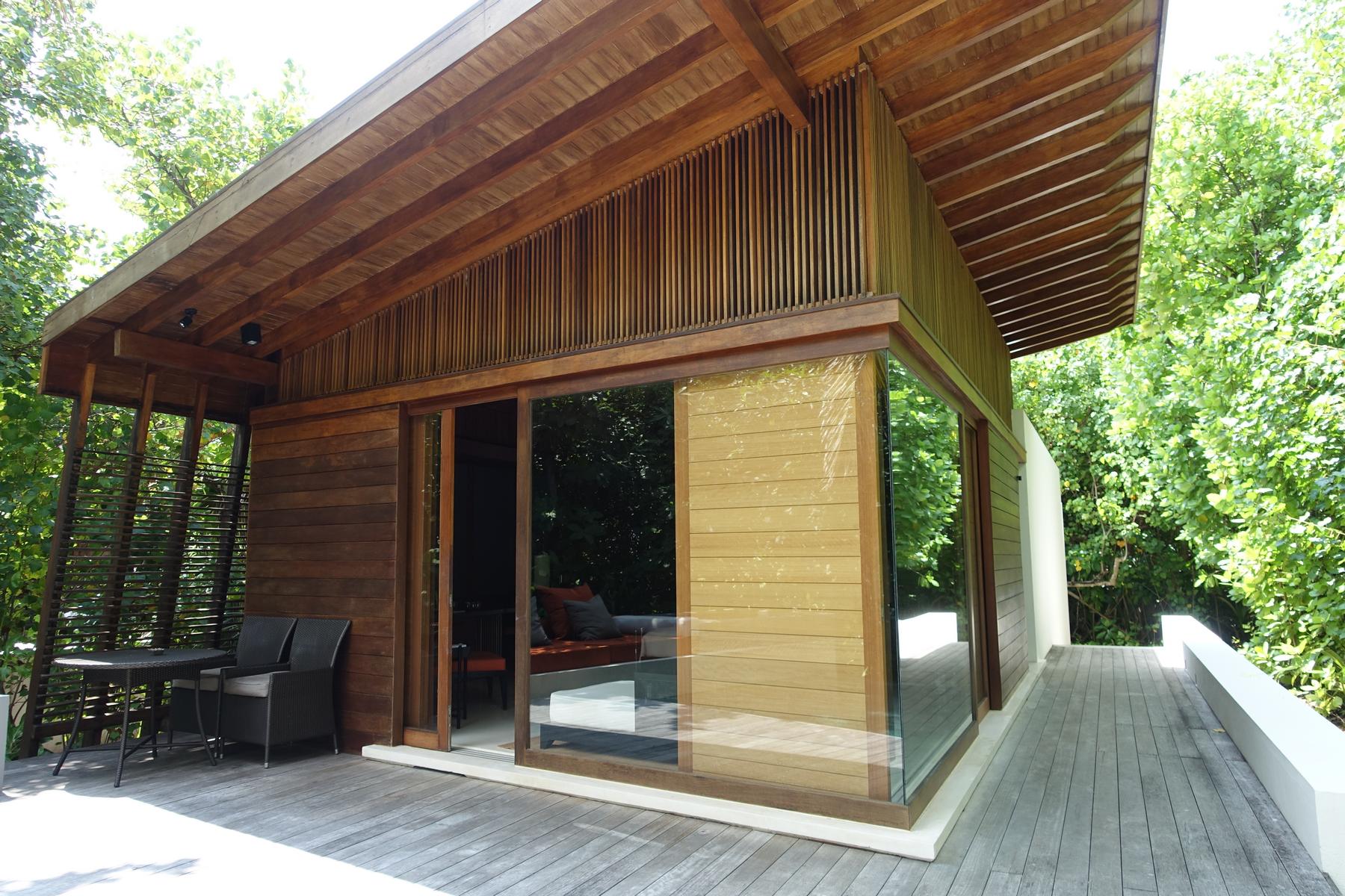 A modern wooden luxury villa with large glass windows and an outdoor deck surrounded by lush greenery.