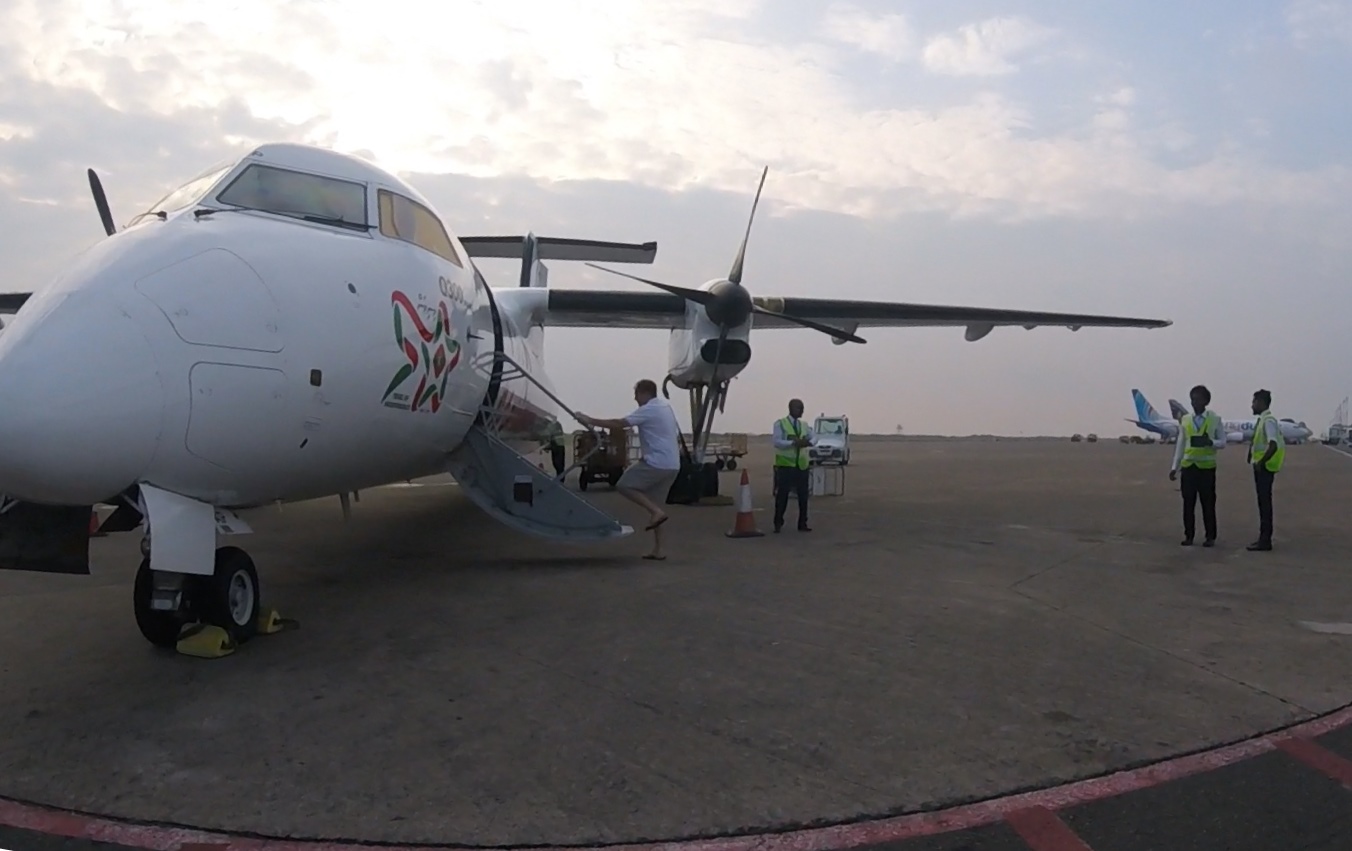 A man boards a Maldivian turboprop plane on an airport tarmac with ground staff.