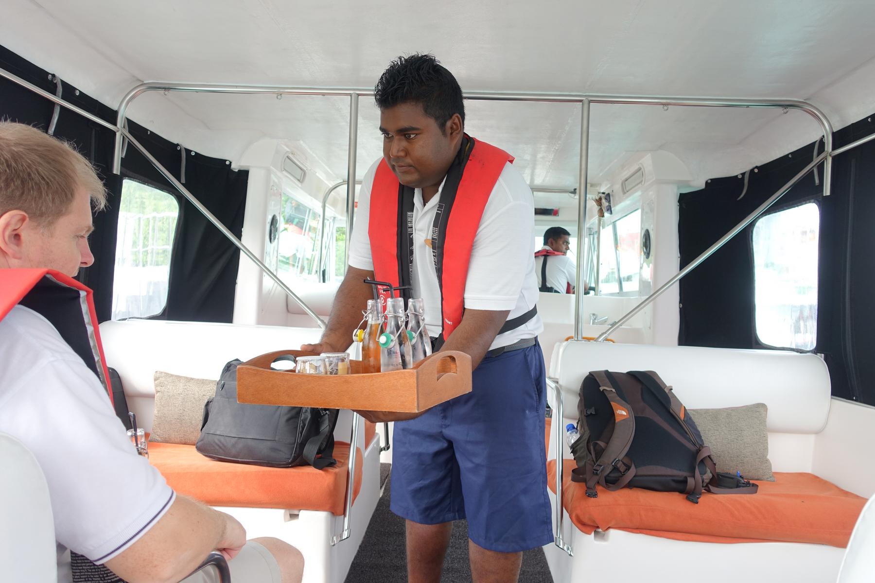 A resort staff member in a life vest serves drinks on a boat to a guest.