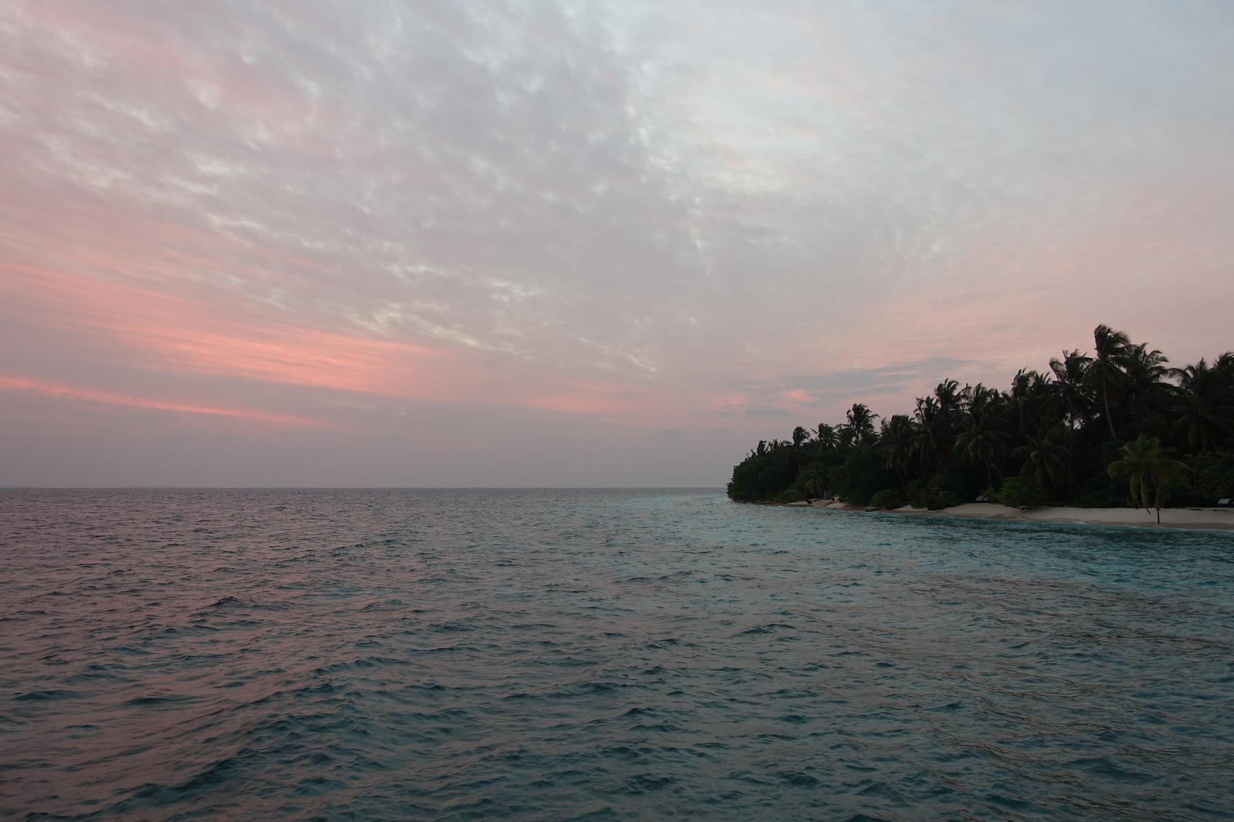 Ocean view with a tropical island under a pink sunset sky.