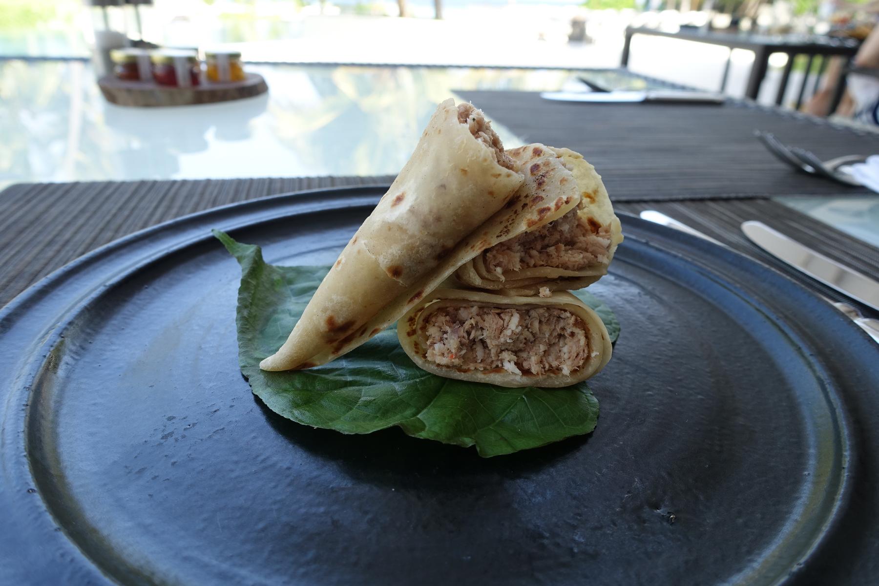 Maldivian flatbread wraps filled with shredded fish, served on a green leaf on a black plate.