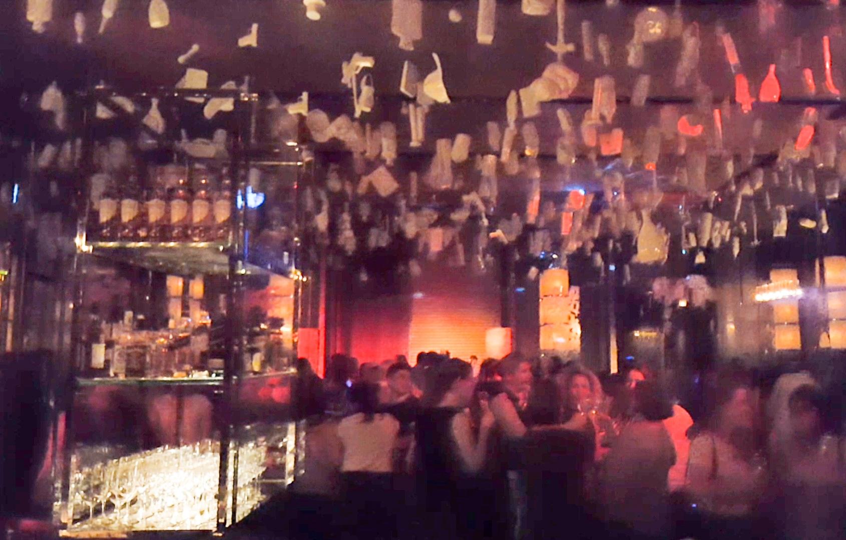 A busy, dimly lit bar with many people socializing and unique white decorations hanging from the ceiling.
