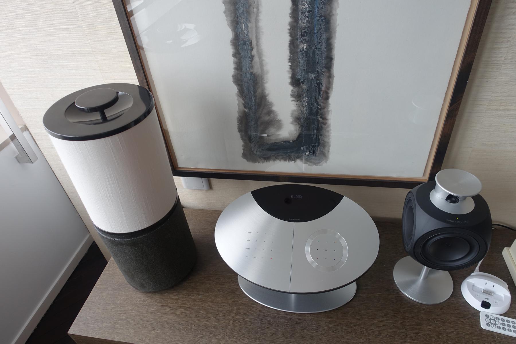 A Bang & Olufsen audio system on a wooden table beneath an abstract painting.