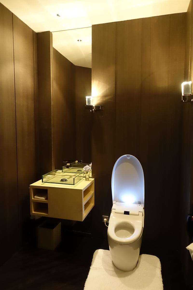 A modern bathroom with dark wood walls features a glass sink, mirror, and an illuminated white bidet toilet.