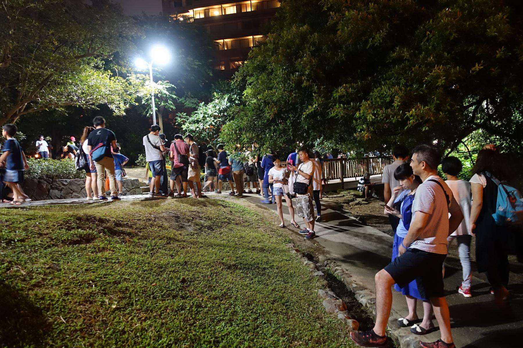 A nighttime crowd of people in a Taiwan park, many focused on their phones for Pokemon Go.