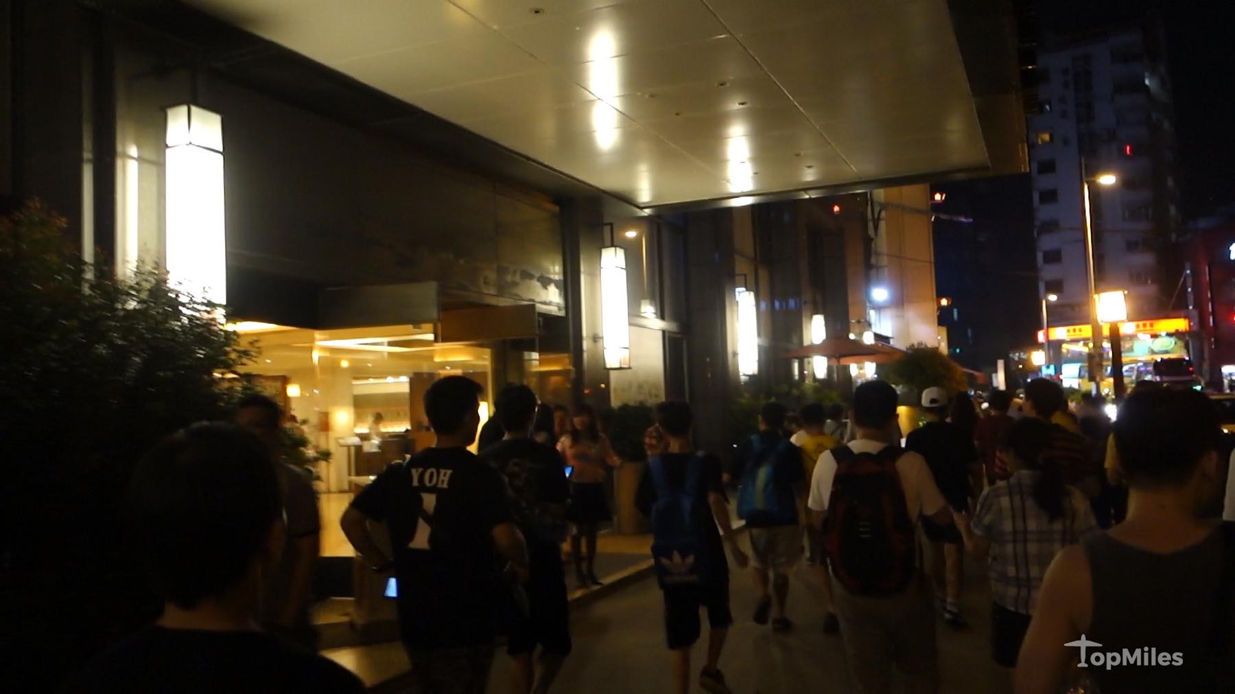 A crowd of people walking quickly down a well-lit city street at night for a Pokemon Go event.