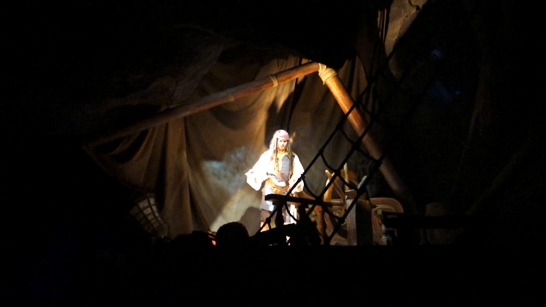 Captain Jack Sparrow animatronic illuminated in a dark scene from the Pirates of the Caribbean ride.