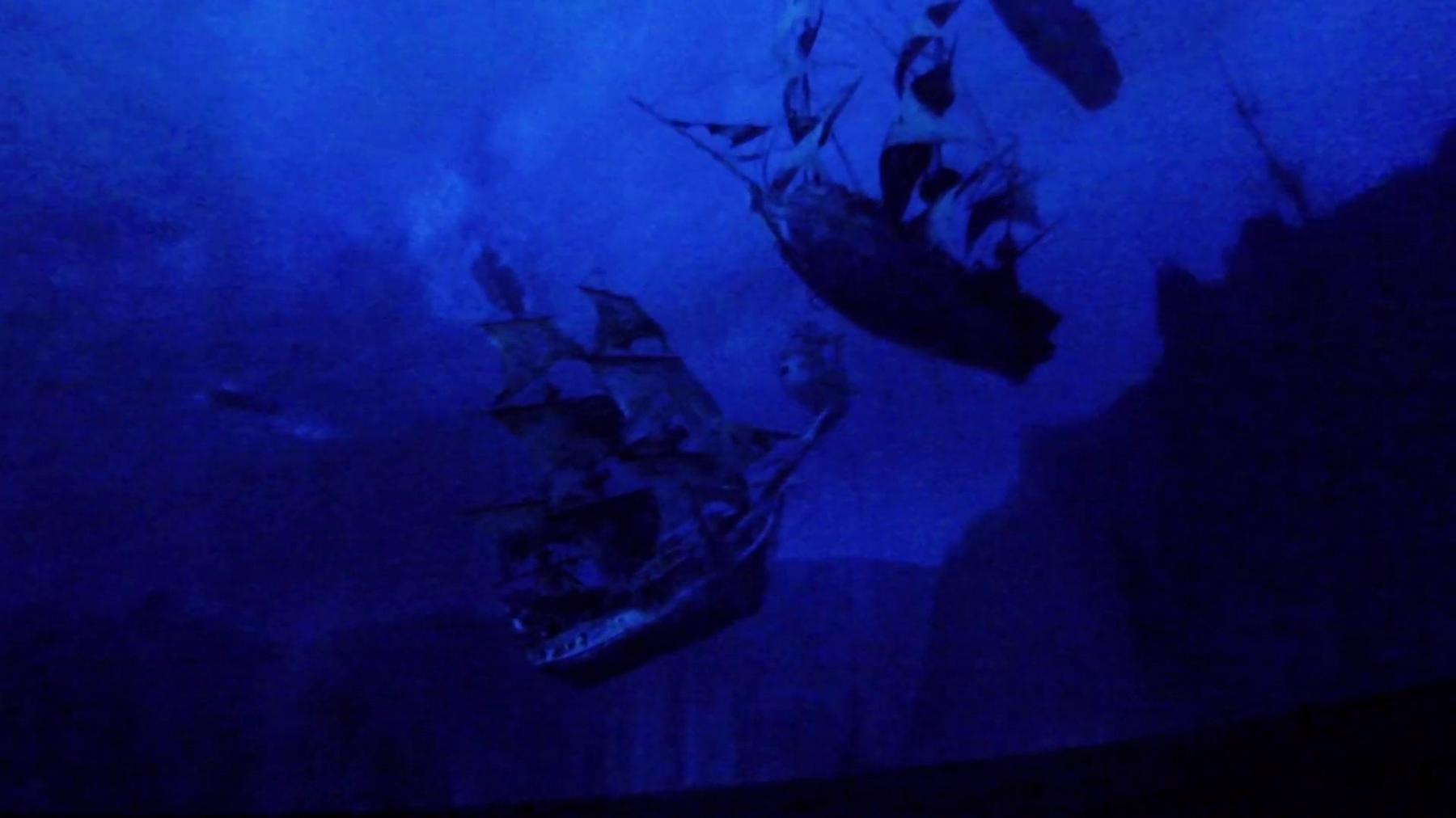 Two ghostly pirate ships are illuminated in a deep blue underwater scene.