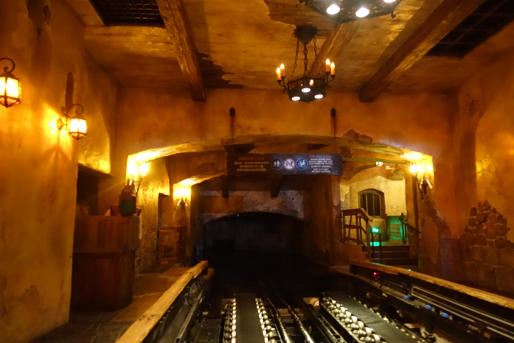 Shanghai Disneyland's Pirates of the Caribbean ride loading area, featuring warm lanterns and tracks disappearing into a dark tunnel.