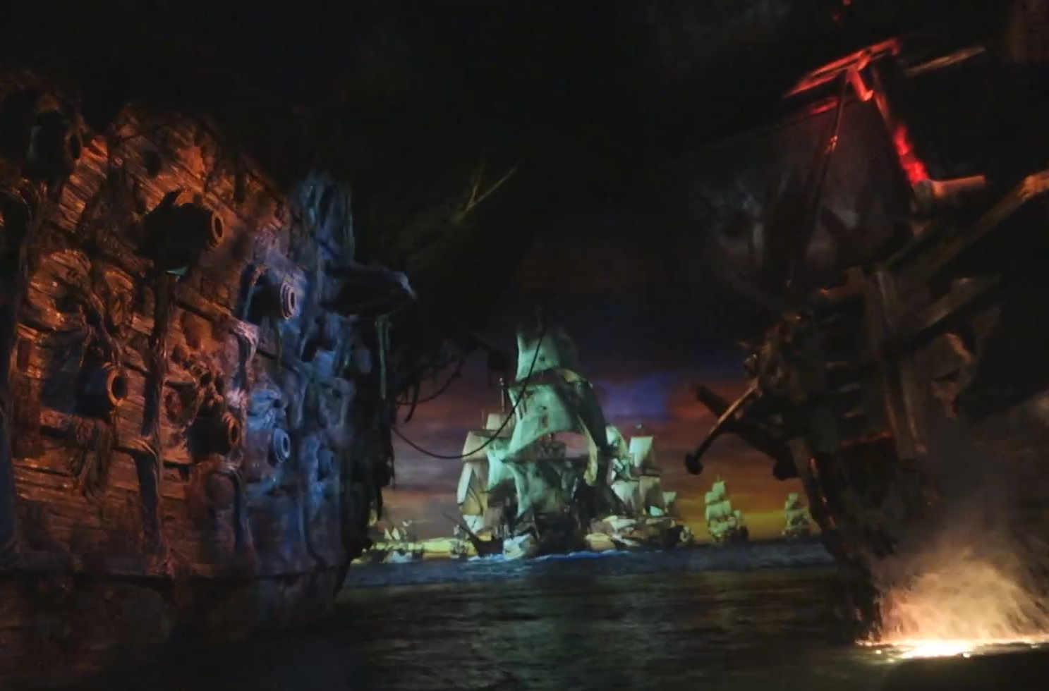 A dark ride scene depicting a projected naval battle between pirate ships with cannon fire effects.