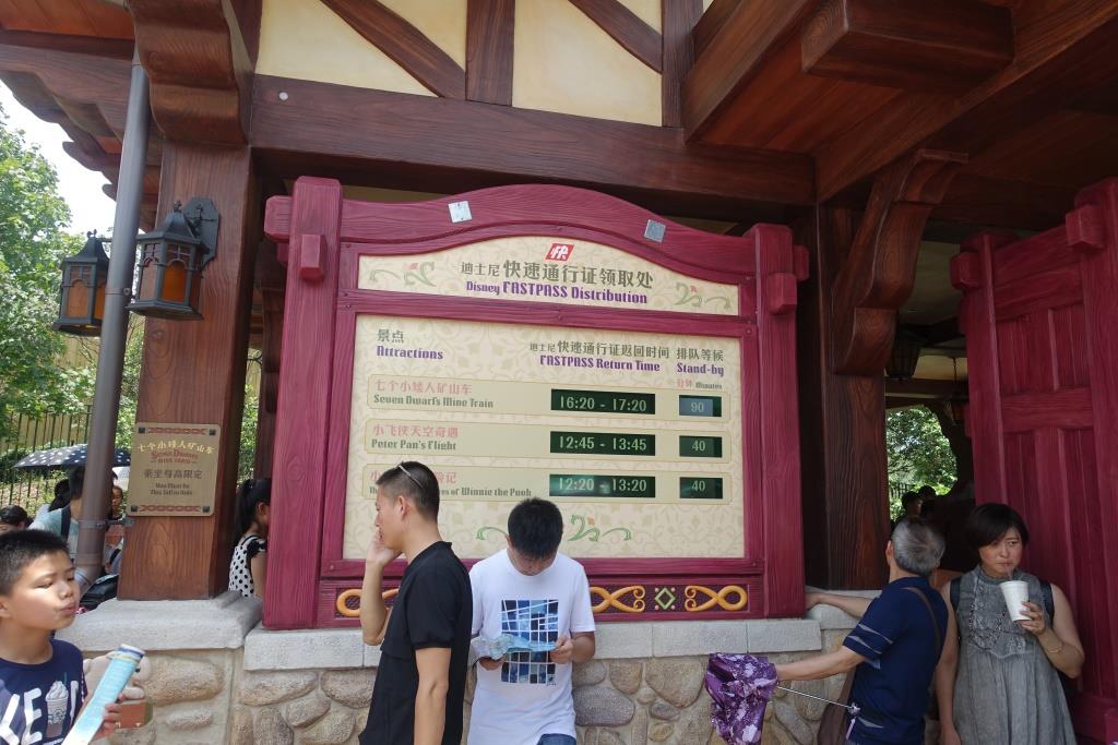 A Disney FASTPASS distribution sign at Shanghai Disneyland displays return times and standby waits for attractions, with guests standing nearby.