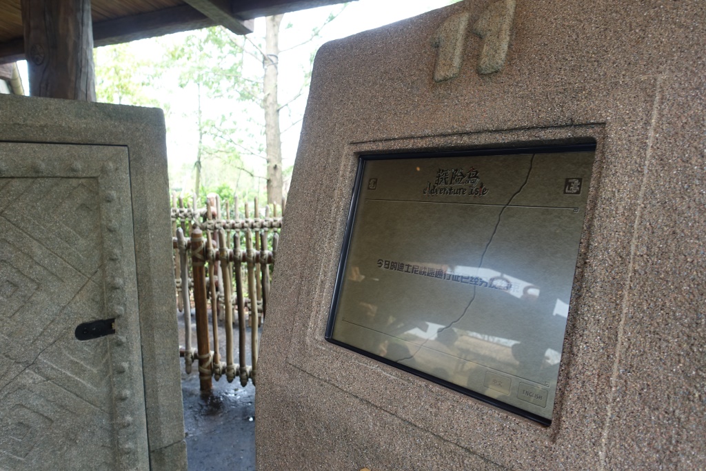 A stone-like information kiosk with a cracked screen showing "Adventure Isle" and Chinese text.