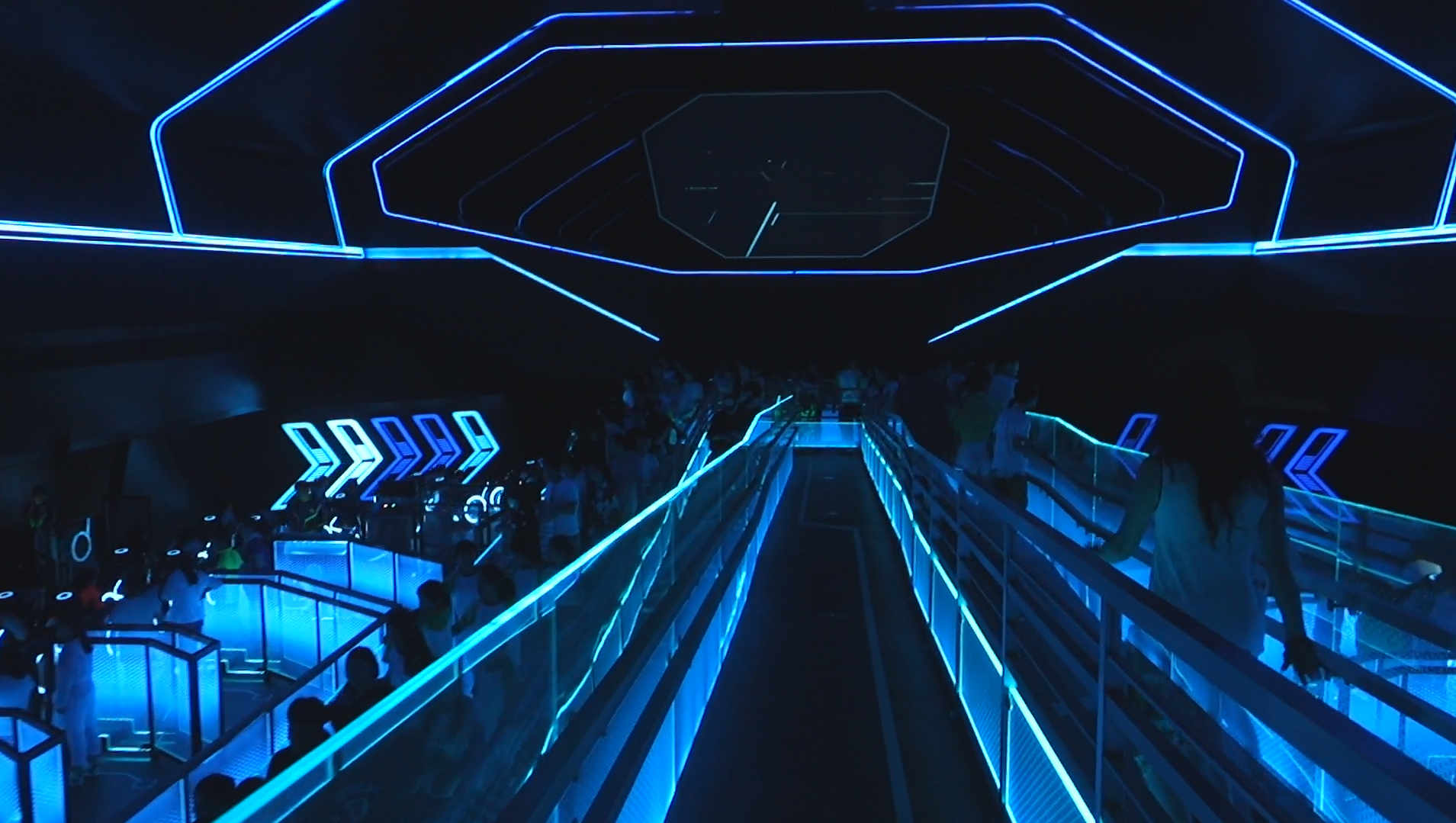 People walking through the dark, blue-lit queue for the TRON LightCycle ride at Shanghai Disneyland.