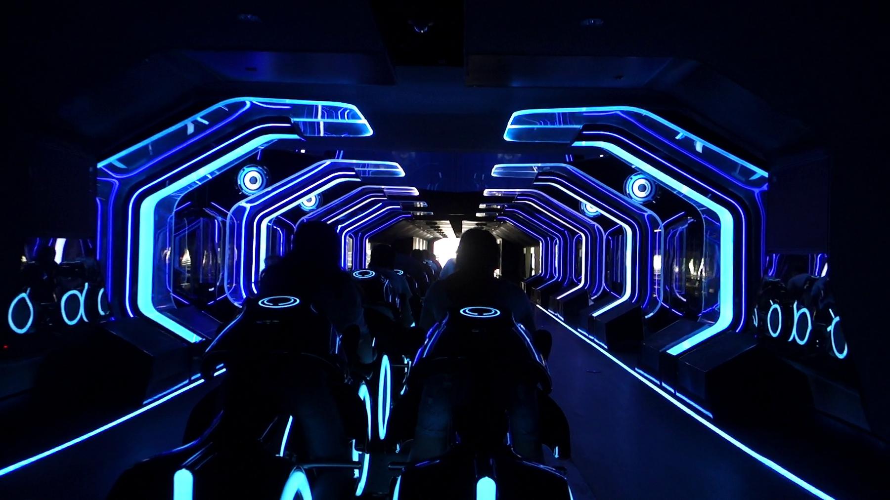 People riding the Tron Lightcycle Power Run attraction in a dark tunnel illuminated by blue neon lights.
