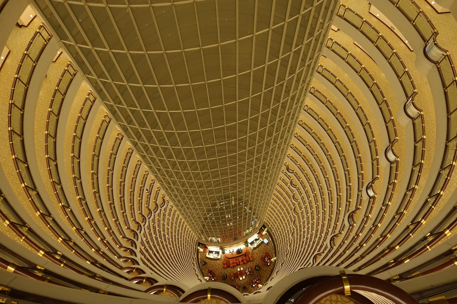 Looking down into a vast, golden hotel atrium with curved balconies and a central glass tower.
