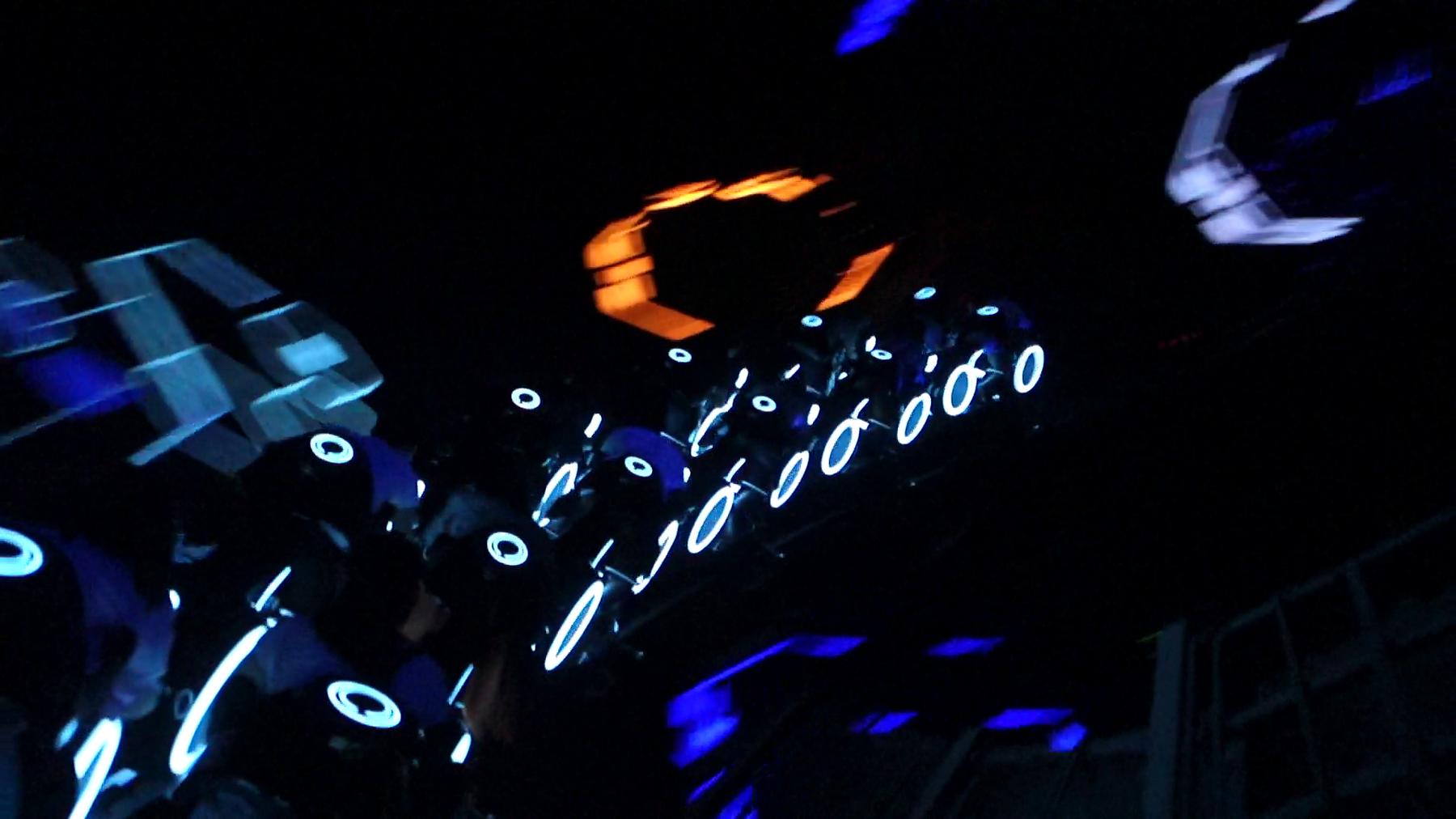 Glowing blue and white vehicles speed through the dark TRON Lightcycle Power Run ride.