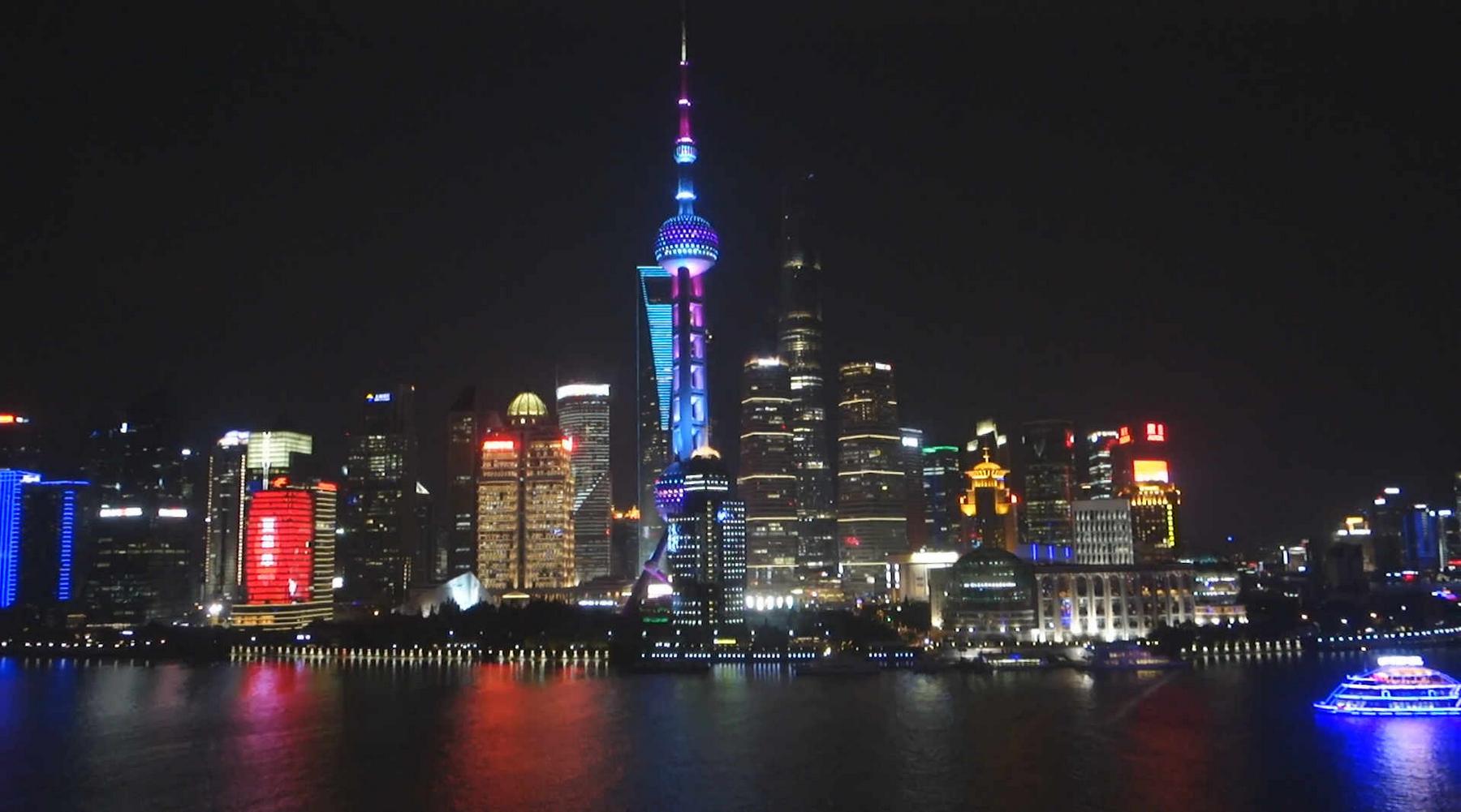 Shanghai skyline at night with the brightly lit Oriental Pearl TV Tower and colorful city lights reflecting on the water.