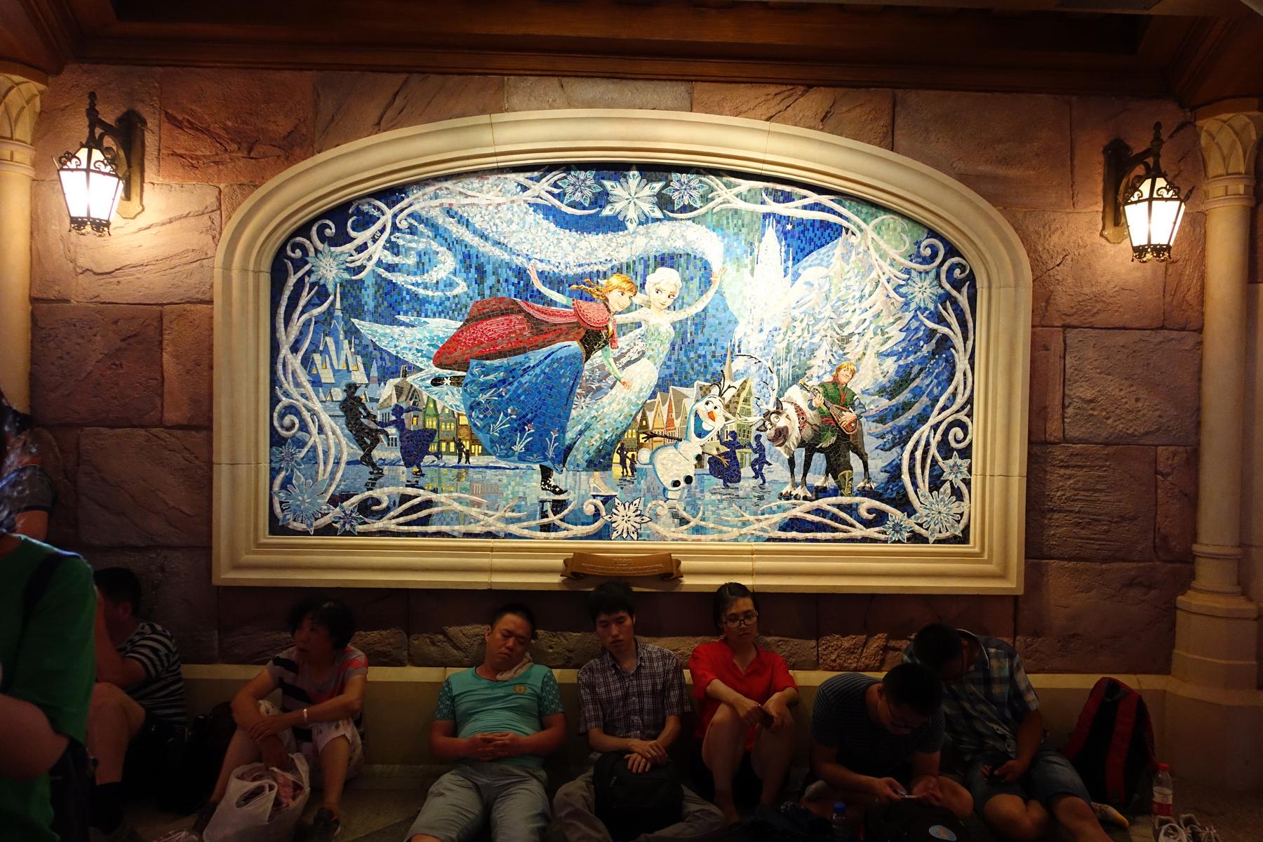 A large "Frozen" mosaic on a stone wall with park visitors resting on the floor below.