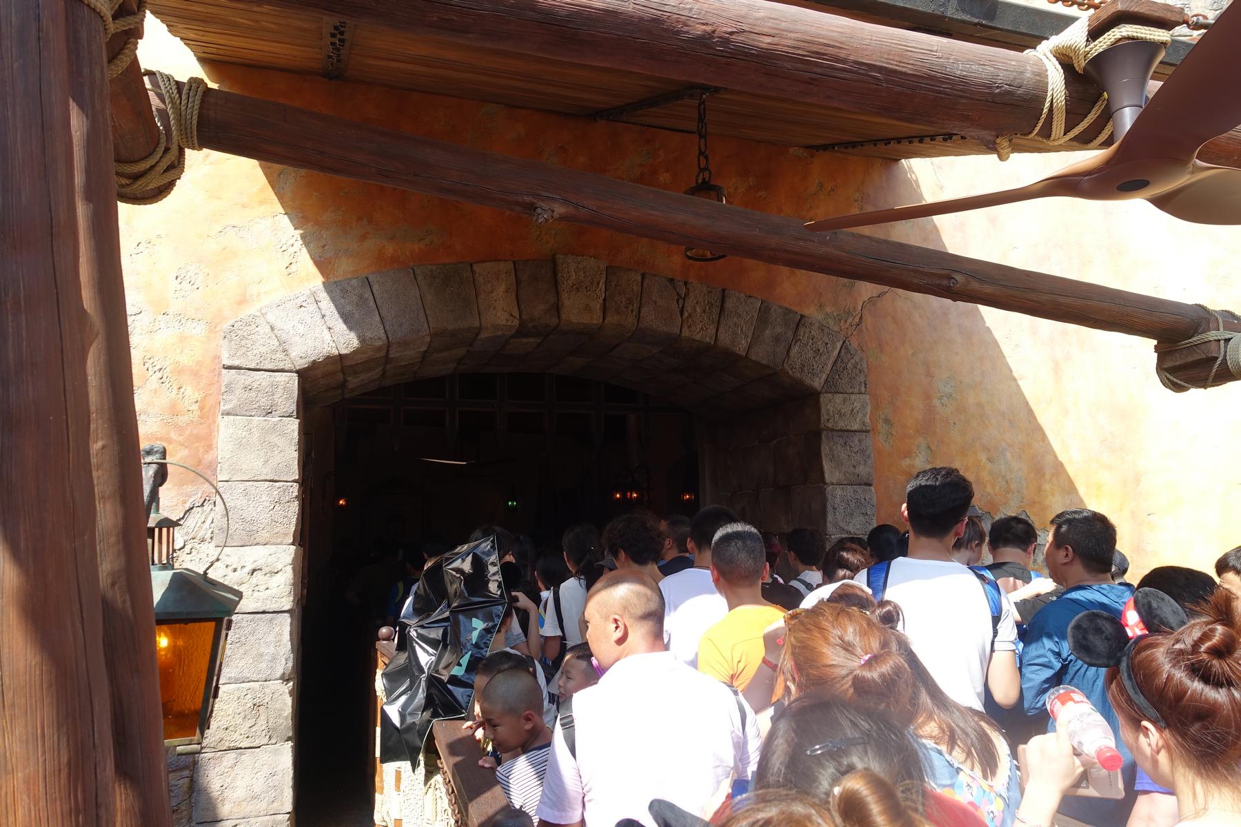 A crowd of people waits in line under a themed archway at Shanghai Disneyland.