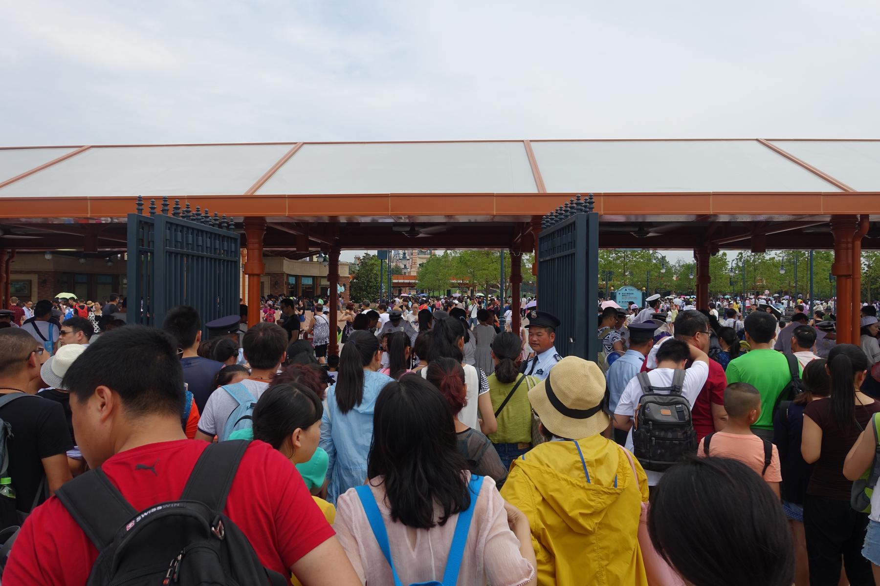 A large crowd of people queuing to enter Shanghai Disneyland through an ornate gate.