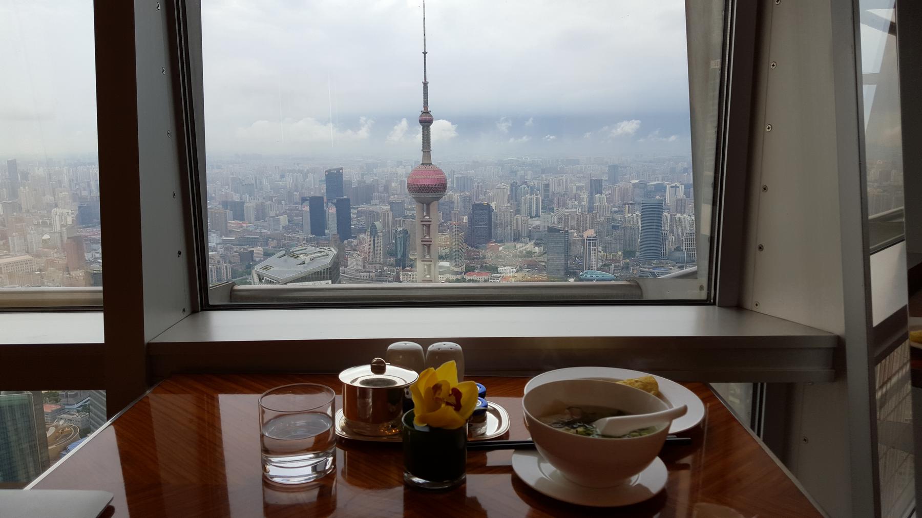A meal on a table overlooks the Shanghai skyline with the Oriental Pearl TV Tower from a high window.