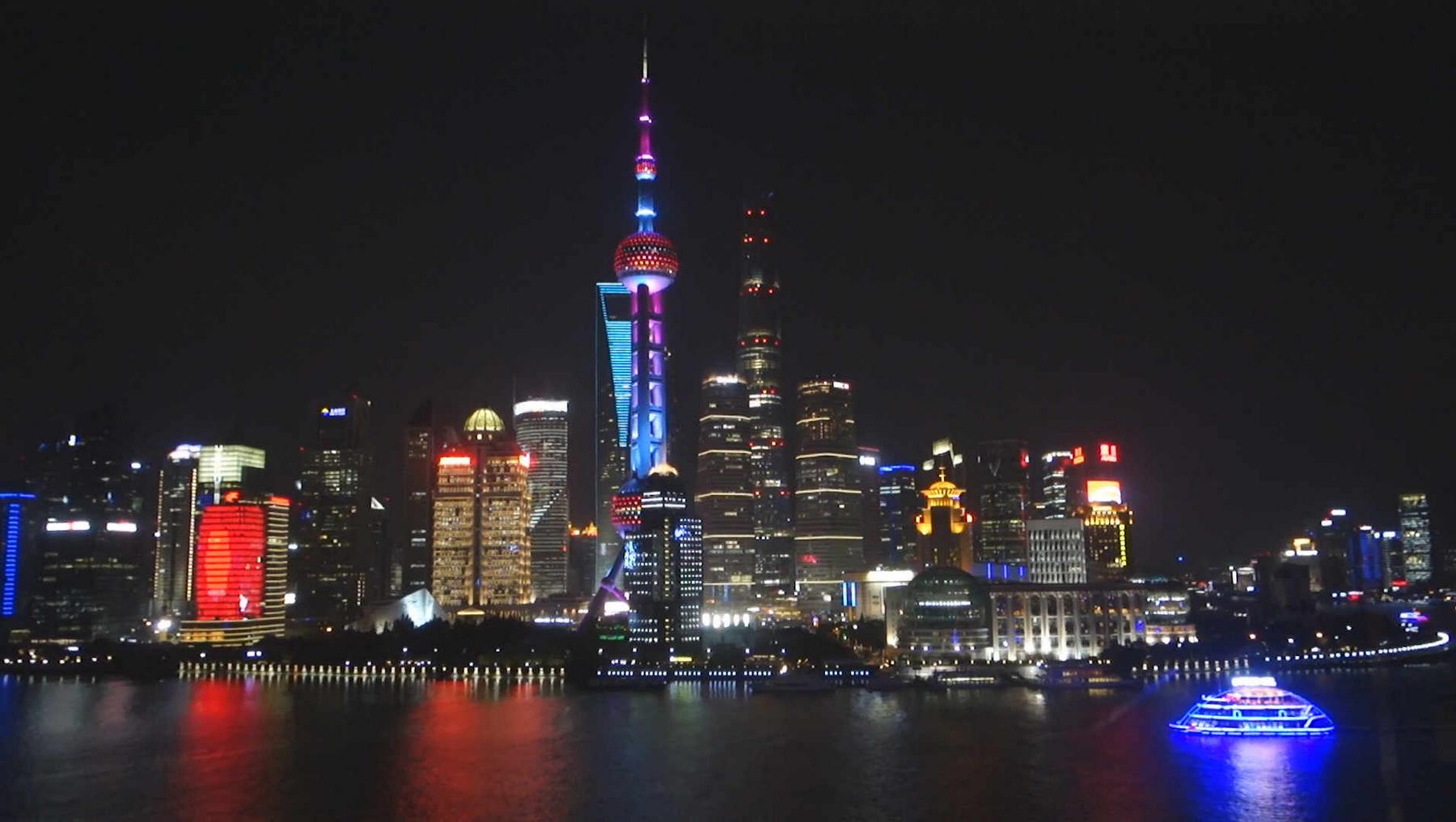 Shanghai skyline at night with the Oriental Pearl TV Tower and a glowing boat on the river.