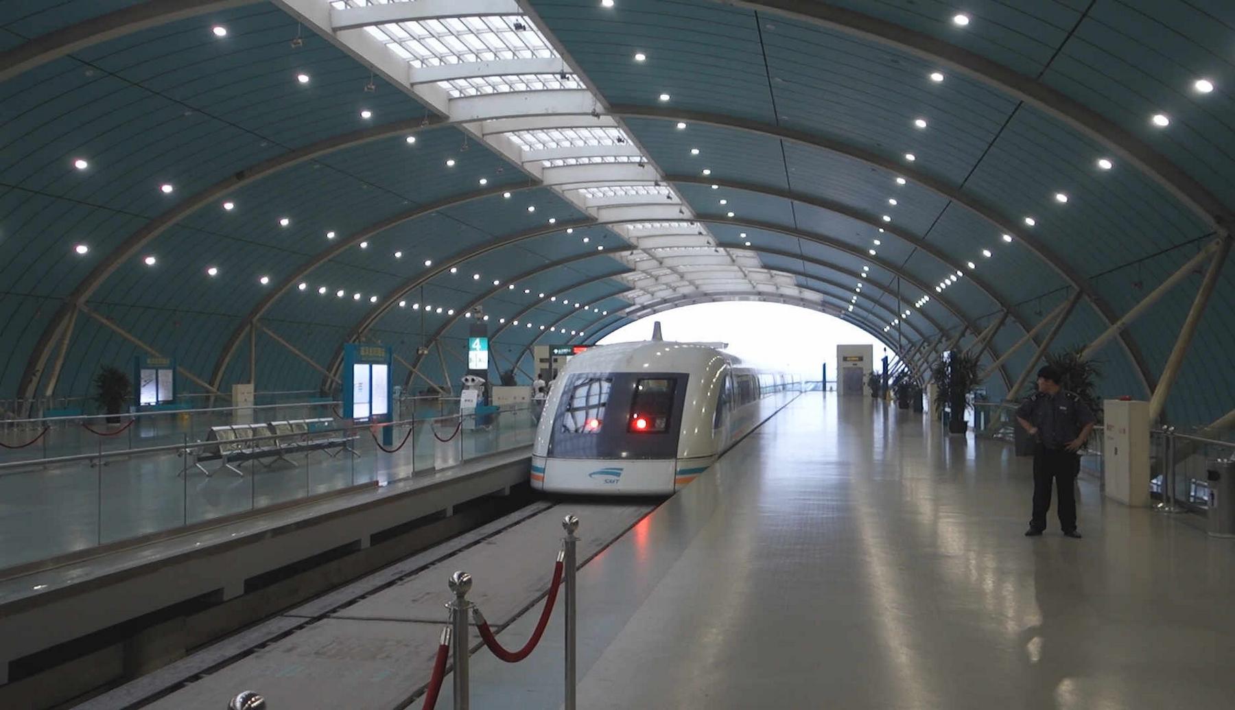 Shanghai Maglev train waiting at a bright, modern station with a staff member on the platform.
