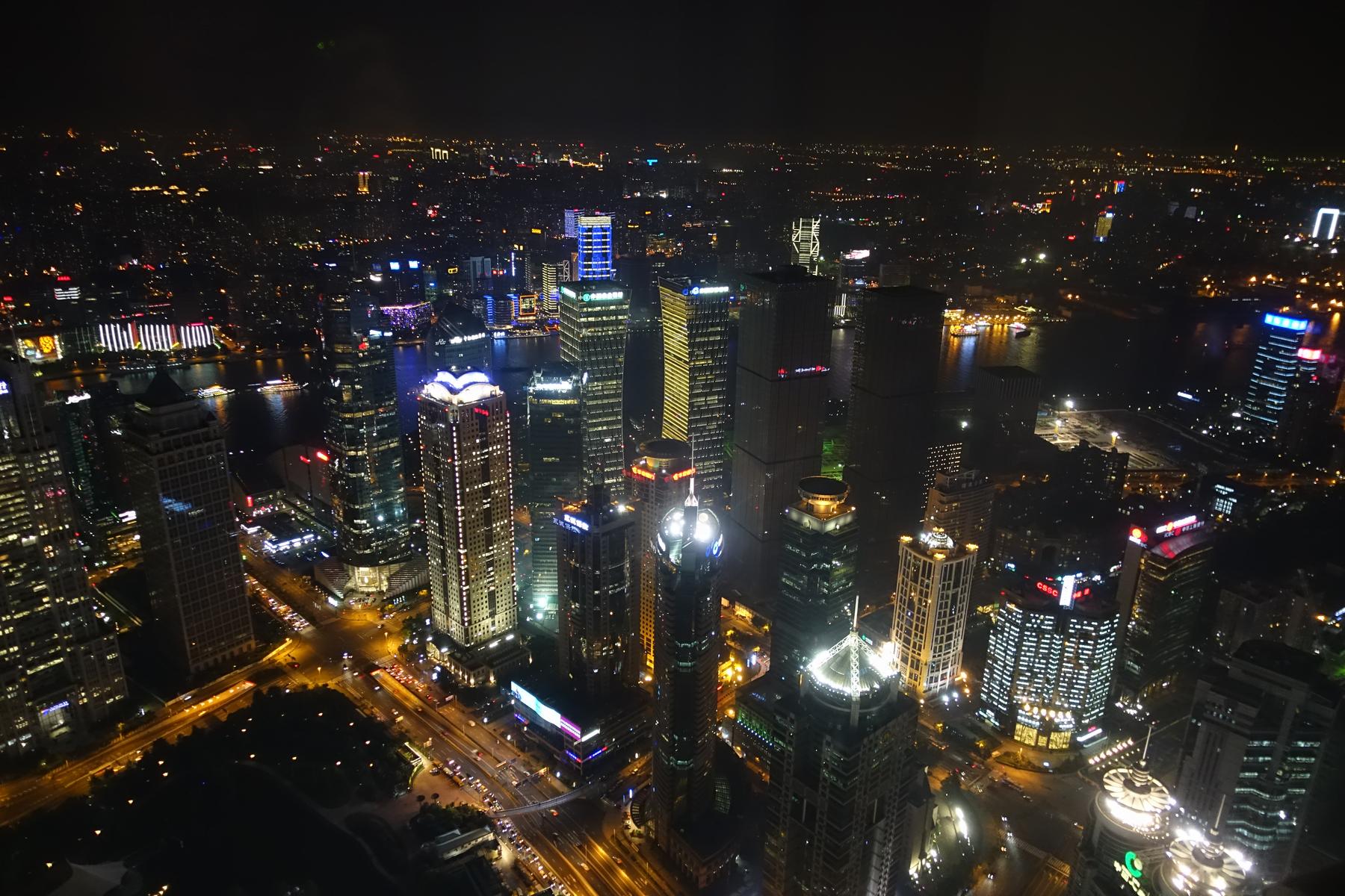 Nighttime aerial view of Shanghai's illuminated skyscrapers and river.