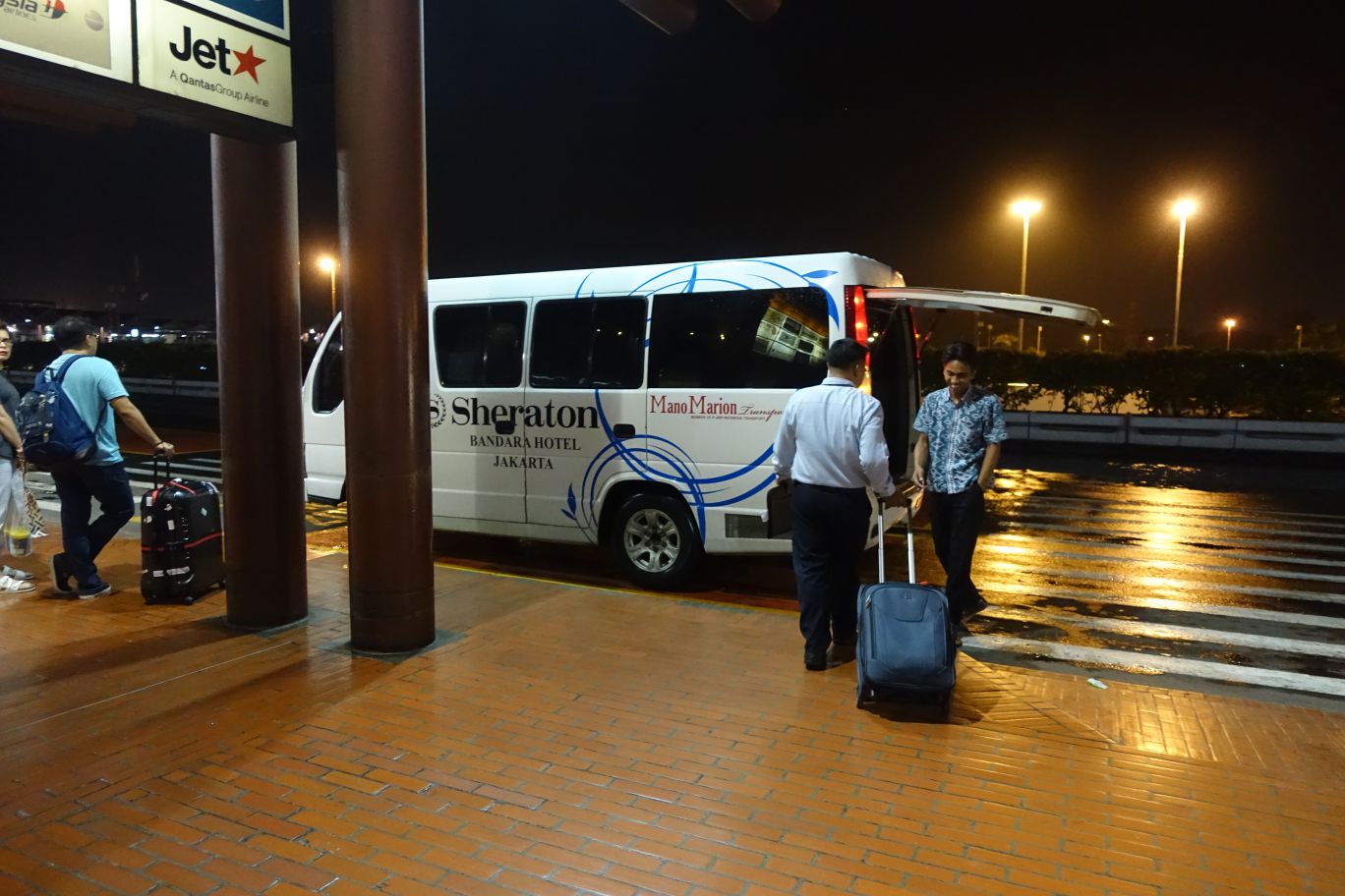 Sheraton Bandara Hotel shuttle bus picking up passengers and luggage at Jakarta Airport at night.