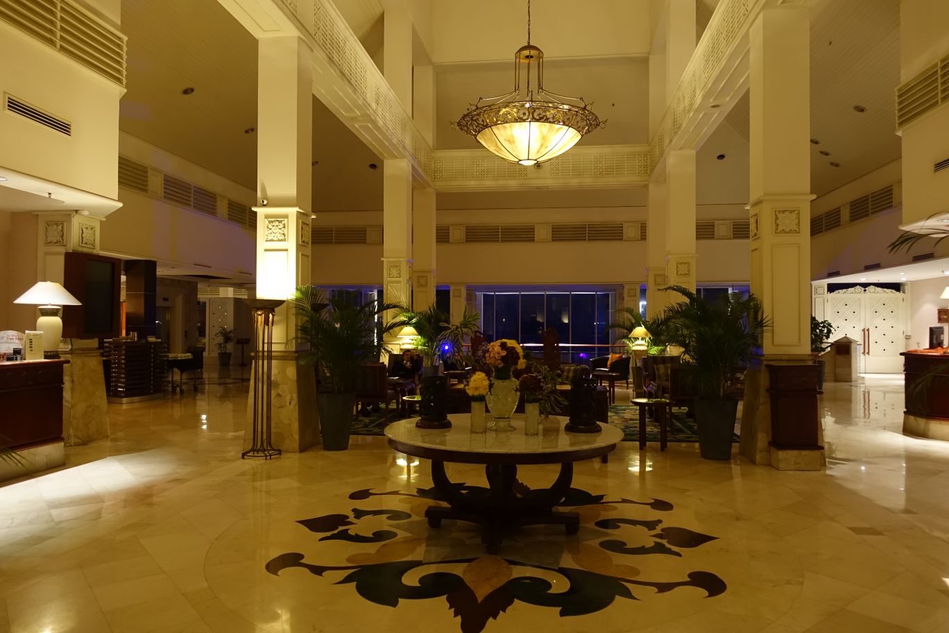 The grand and warmly lit lobby of the Sheraton Bandara hotel, featuring a patterned floor and large chandelier.