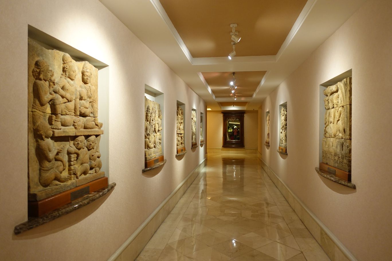 A hotel hallway featuring ornate carved stone reliefs embedded in illuminated wall niches.
