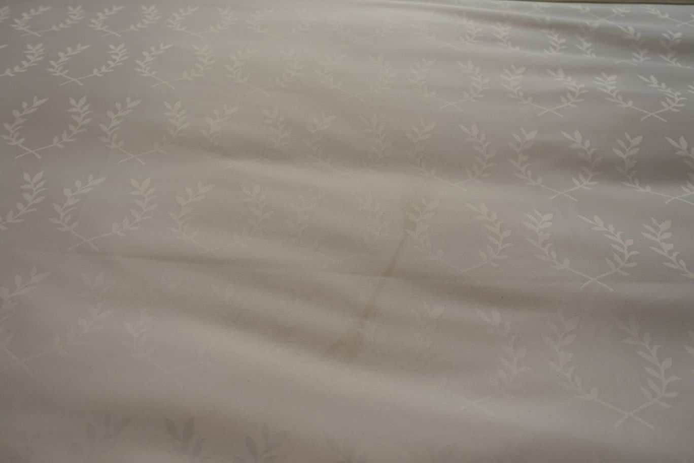 Light-colored hotel bed linen with a subtle repeating pattern of leaf sprigs.