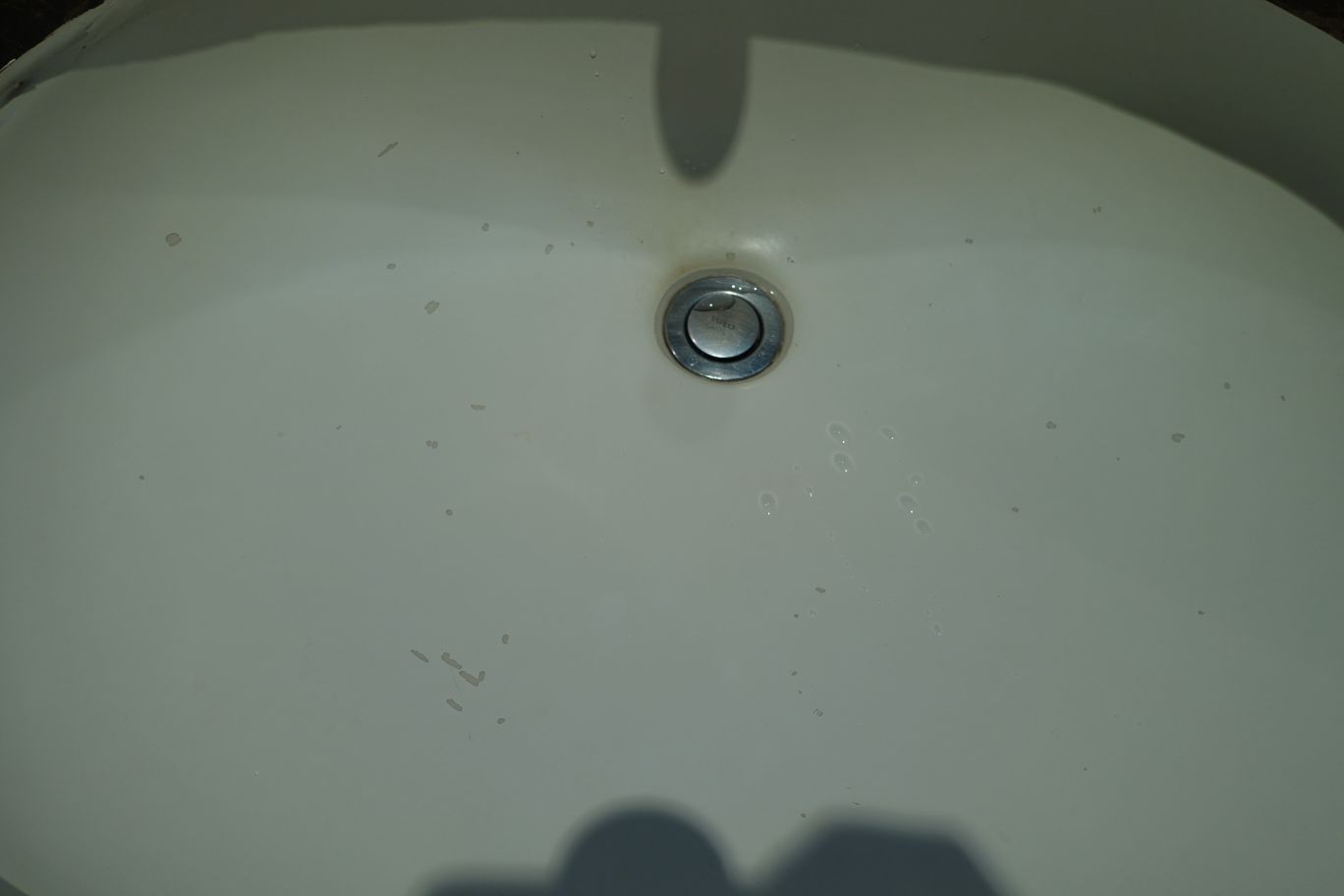A white sink basin with a metal drain and visible marks and water spots.