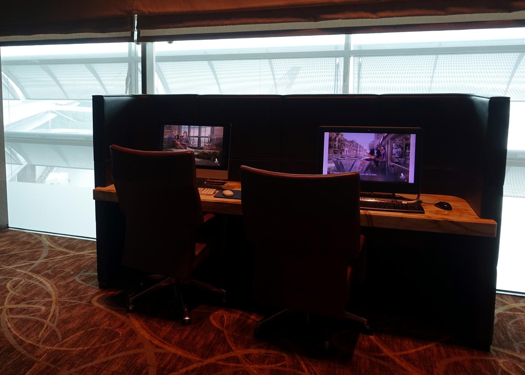 Two computer workstations with dark brown leather chairs in a modern lounge with large windows.