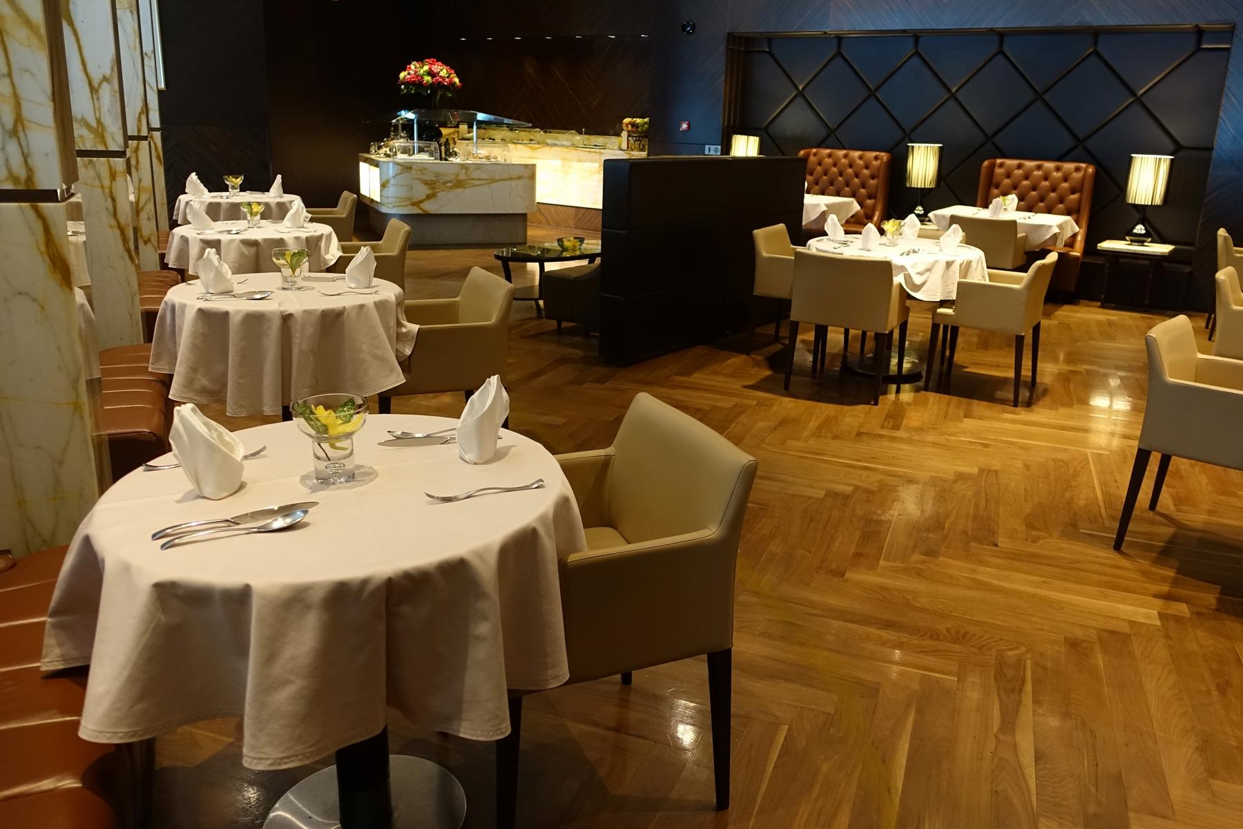 An elegant first-class lounge dining area with tables set for meals and plush seating.