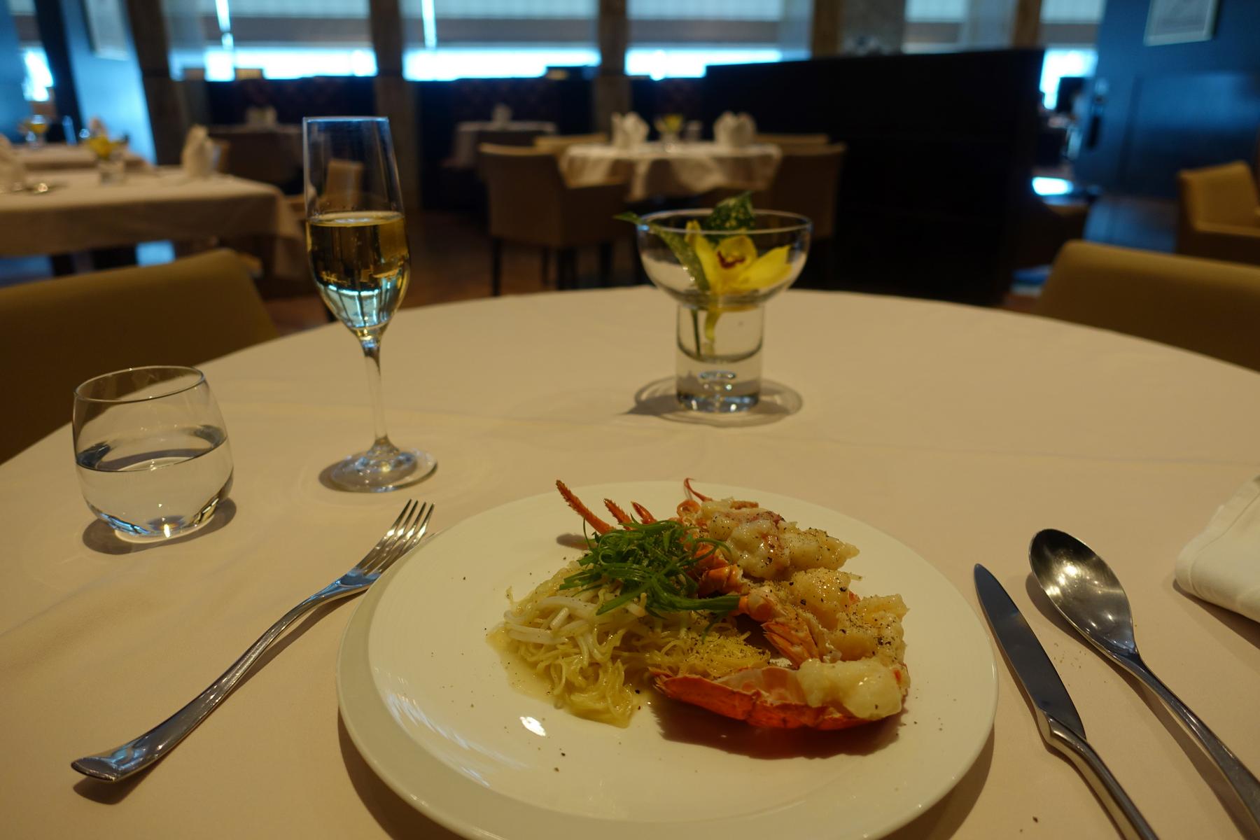 A plate of lobster and noodles with champagne and water on an elegant dining table.