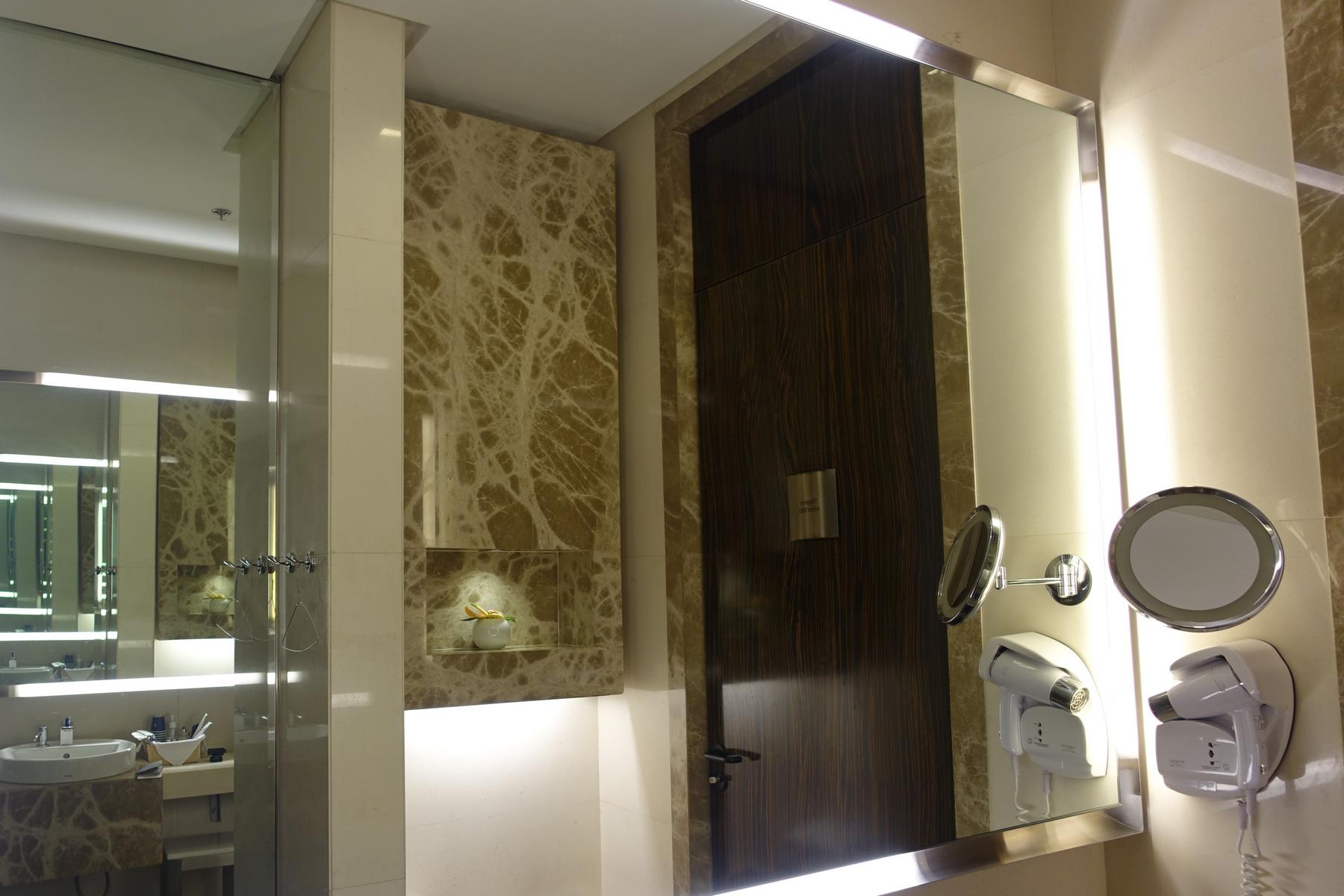 Luxurious bathroom with veined marble walls, a large mirror, a dark wood door, and wall-mounted hair dryers.
