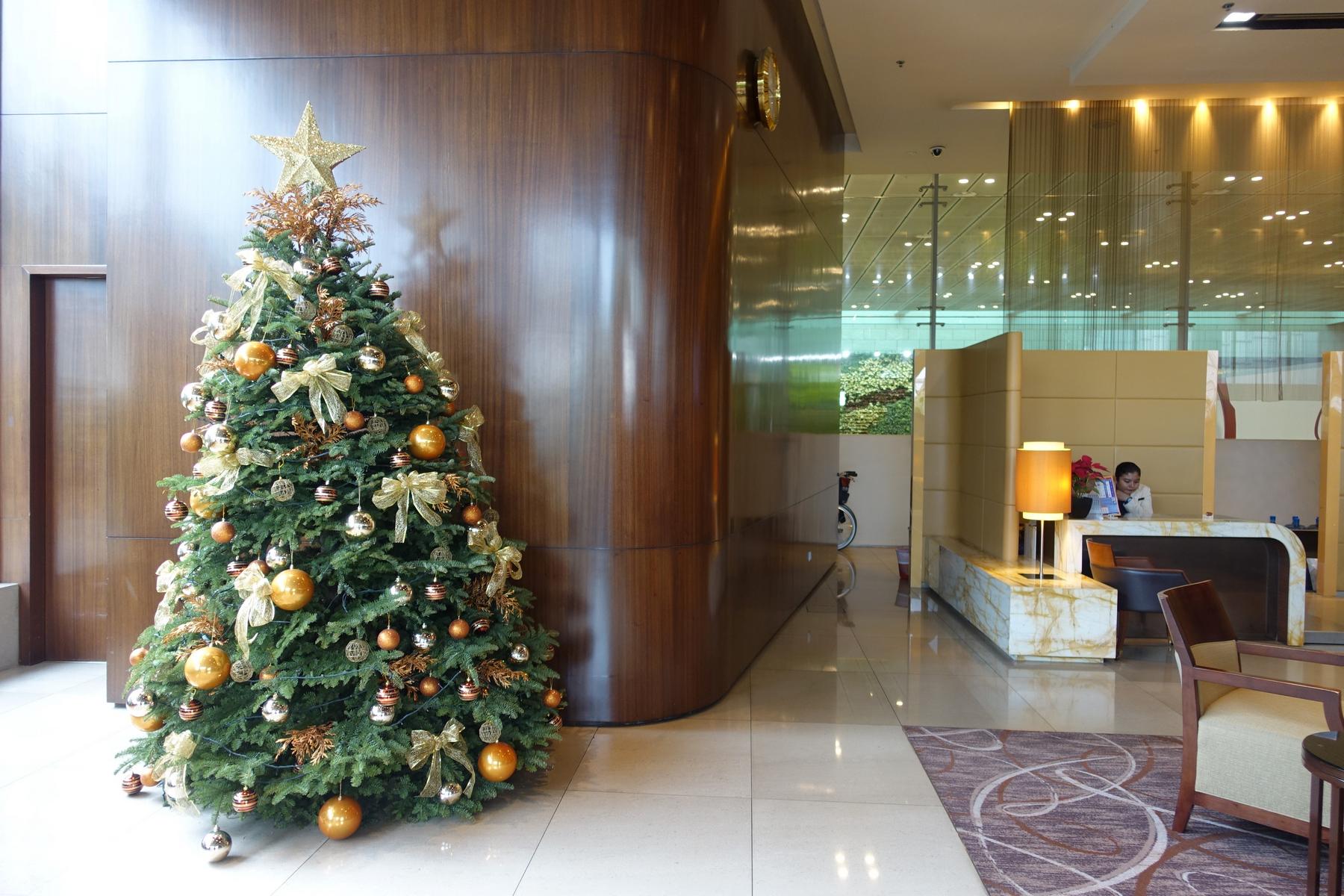 A festive Christmas tree with gold and bronze ornaments in a modern airport lounge with a receptionist.