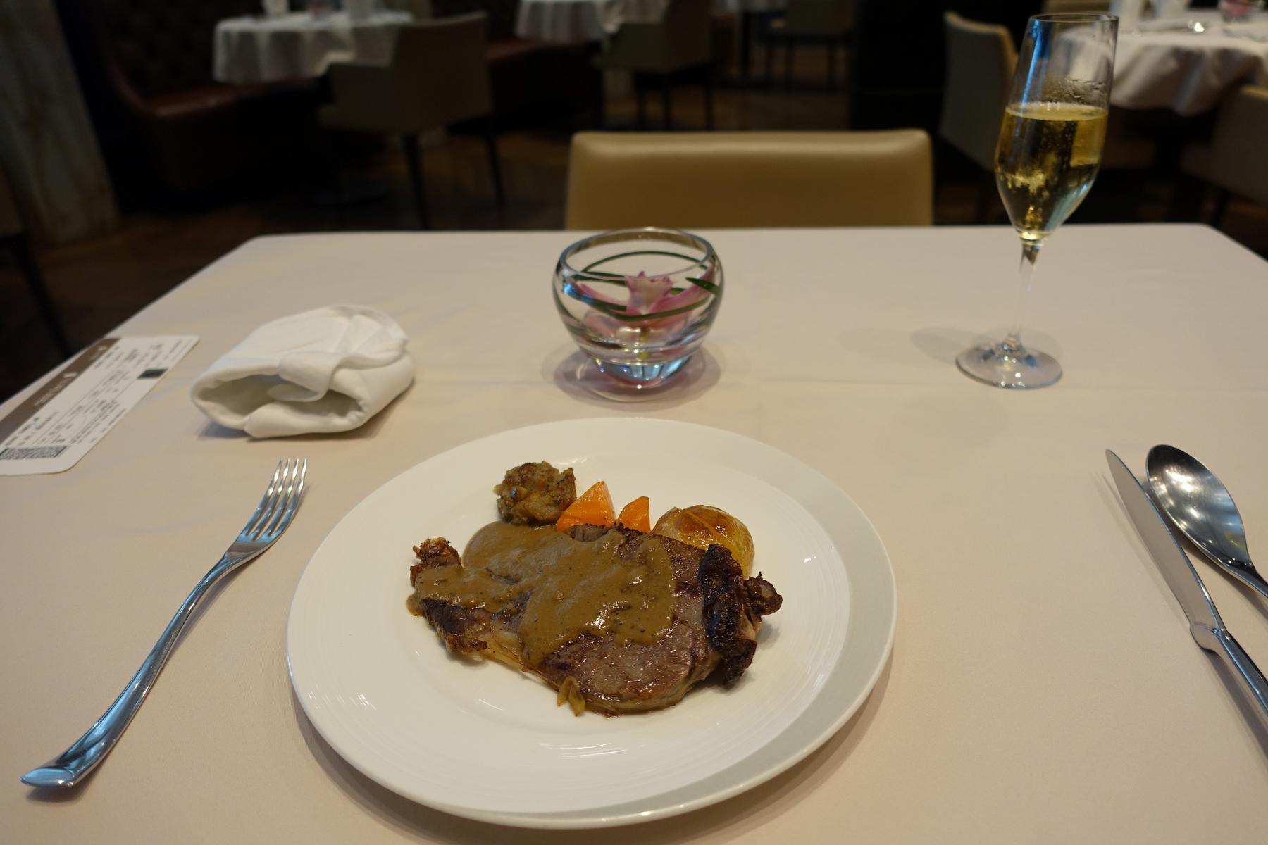 A steak dinner with roasted vegetables and champagne served on a white tablecloth.