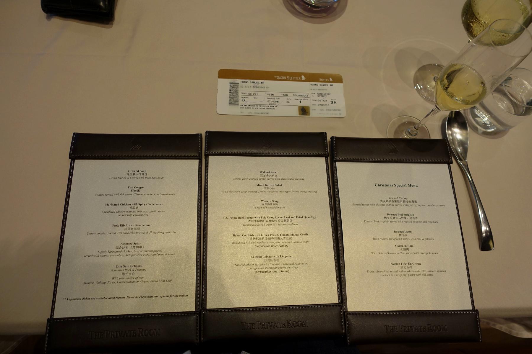 Three menus from "The Private Room," a Singapore Airlines boarding pass, and a glass of champagne on a table.