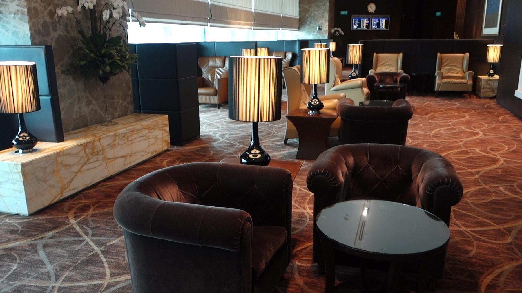 A luxurious airport lounge with comfortable armchairs, stylish lamps, and a patterned carpet.