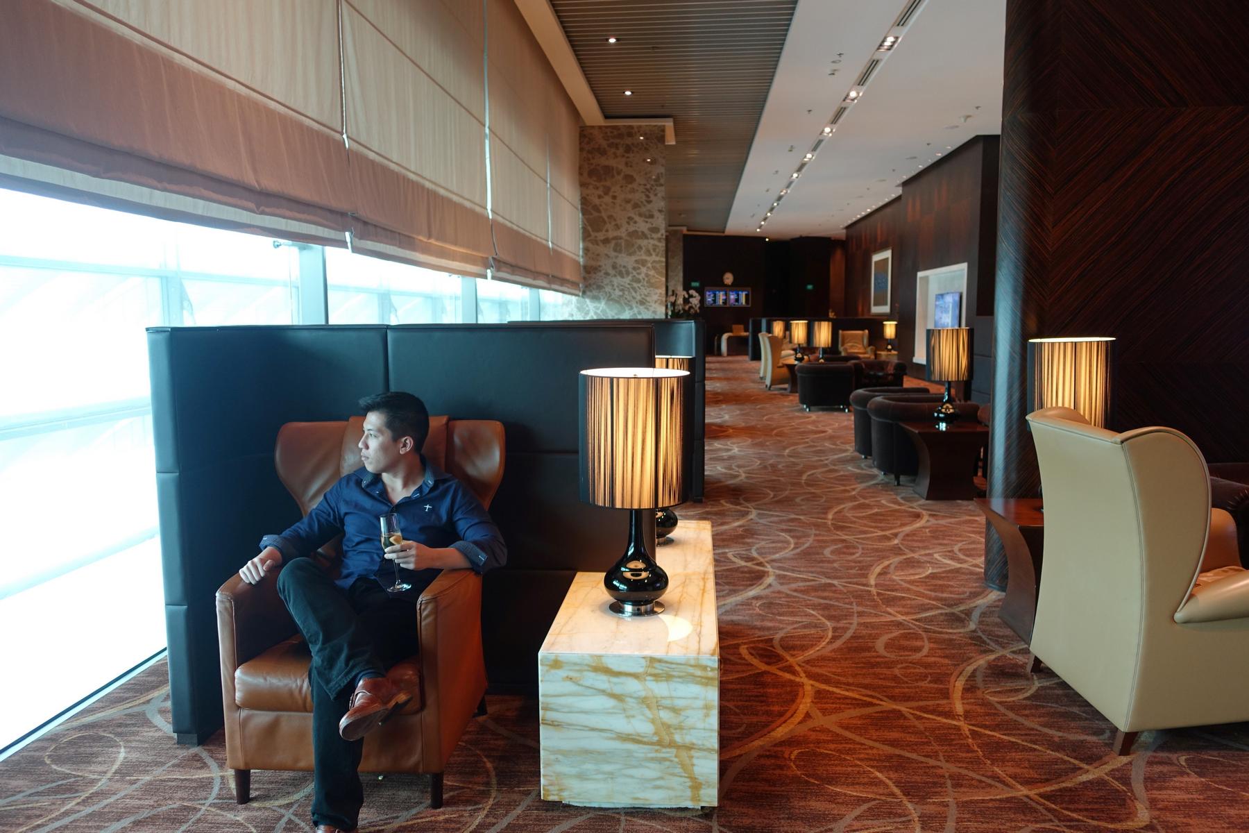 A man relaxes in a luxurious lounge, sipping a drink and looking out a large window.