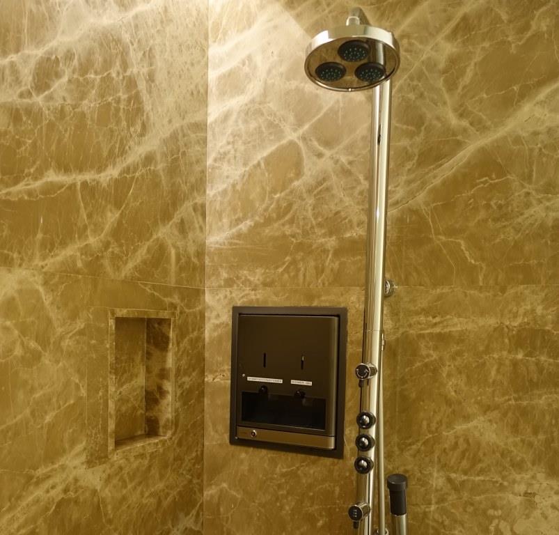 A modern shower stall featuring tan marble walls, a chrome rain shower head, and a built-in amenity dispenser.