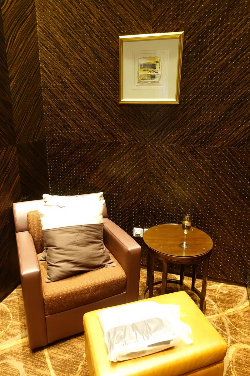 A luxurious seating area with a brown armchair, a small table with a champagne flute, and a golden ottoman.