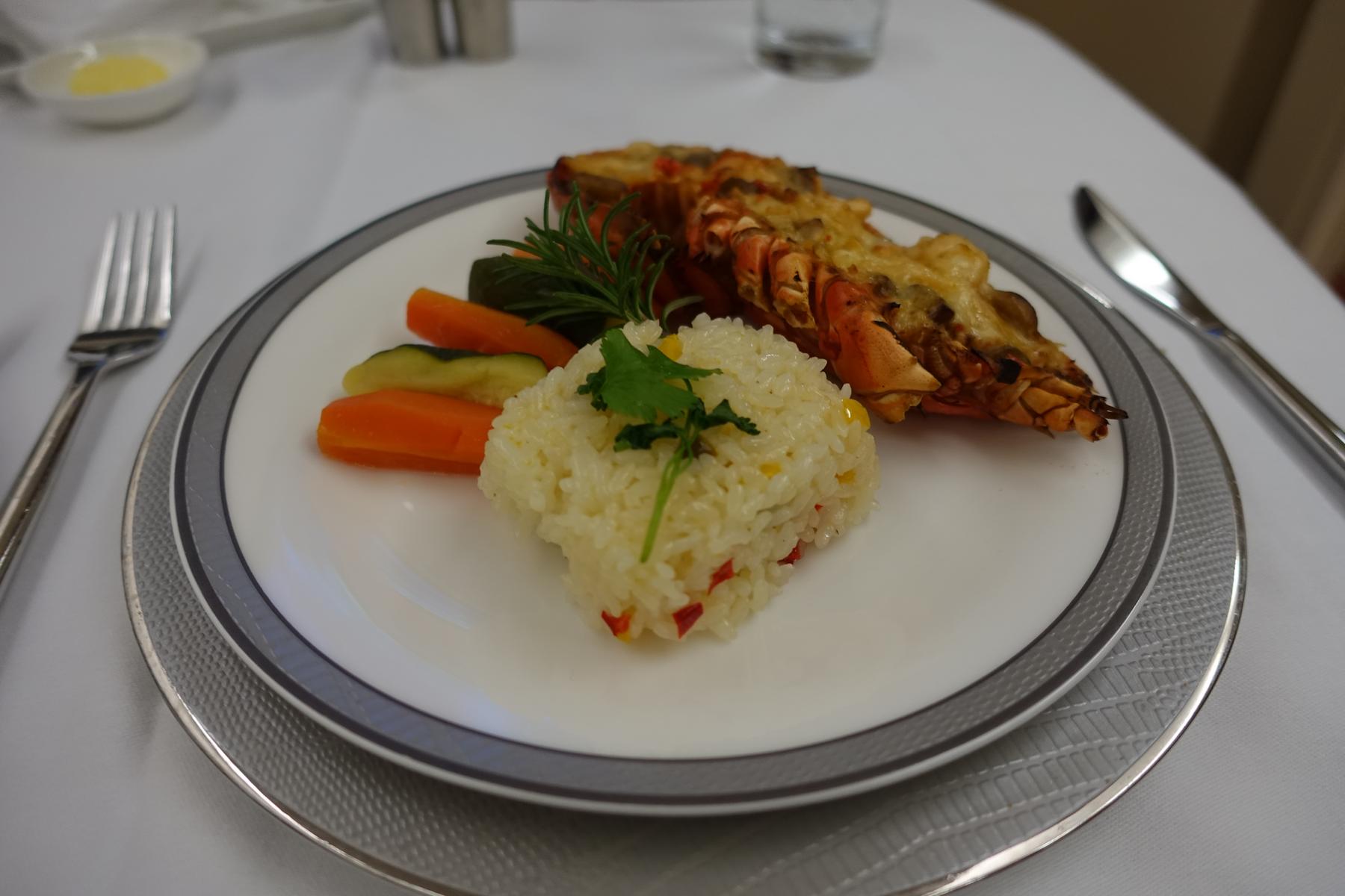 A beautifully presented meal of cooked lobster, a molded rice mound, carrots, and cucumber on a white plate.