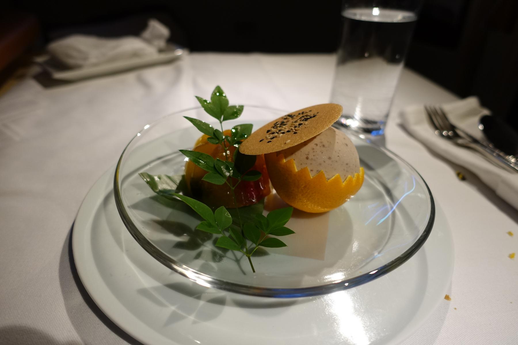 A beautifully presented dessert of ice cream in an orange peel, a sesame wafer, and fruit jelly, garnished with fresh leaves.