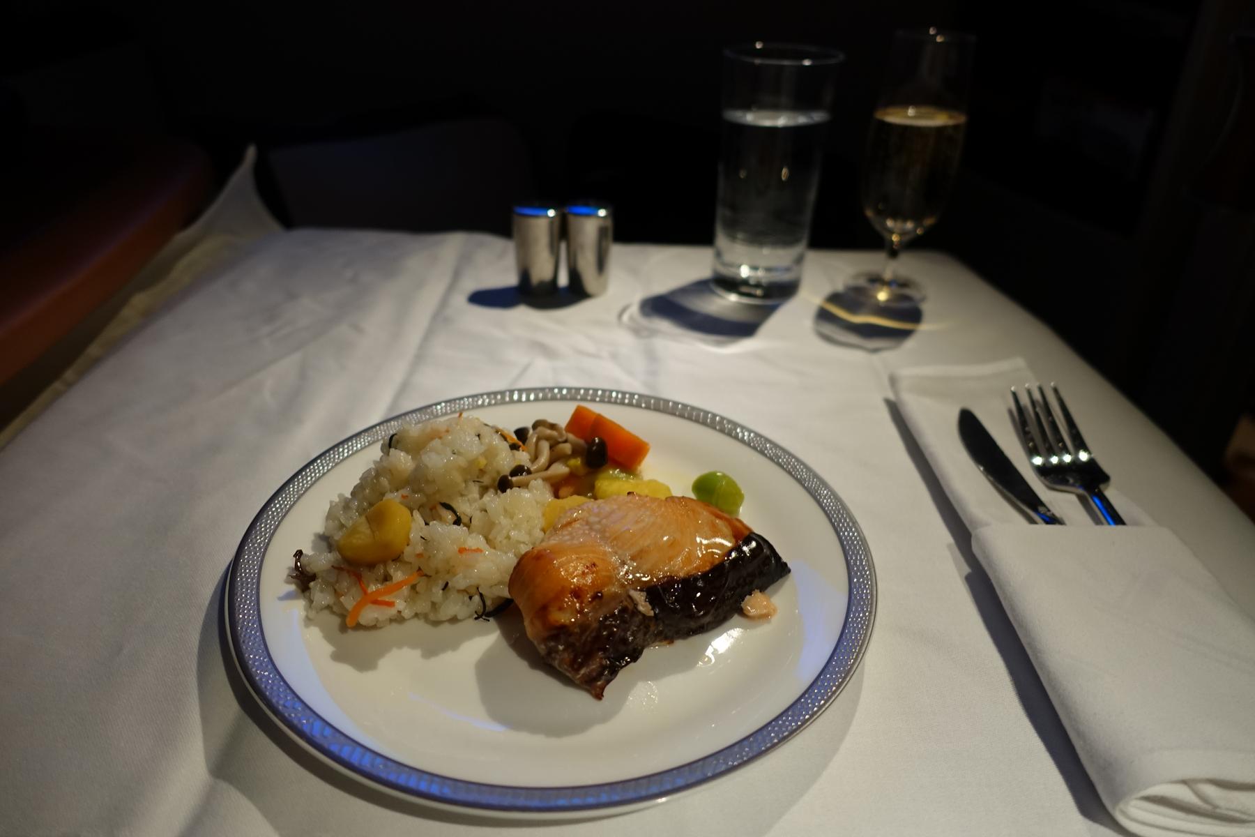 A Singapore Airlines Suites Class meal with salmon, rice, and champagne served on a white tablecloth.