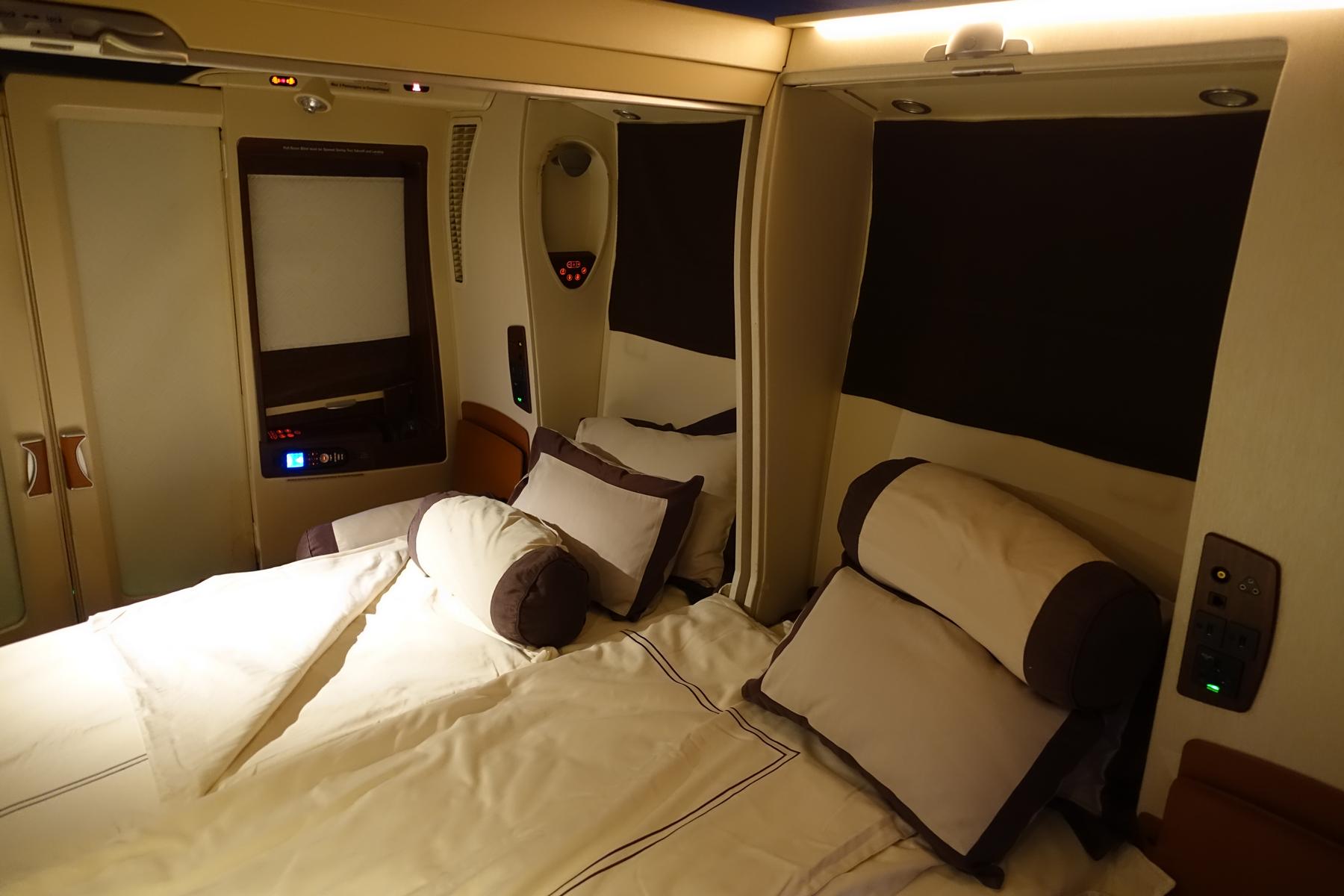 A luxurious bed with white linens and brown-trimmed pillows set up in a private Singapore Airlines Suites cabin.