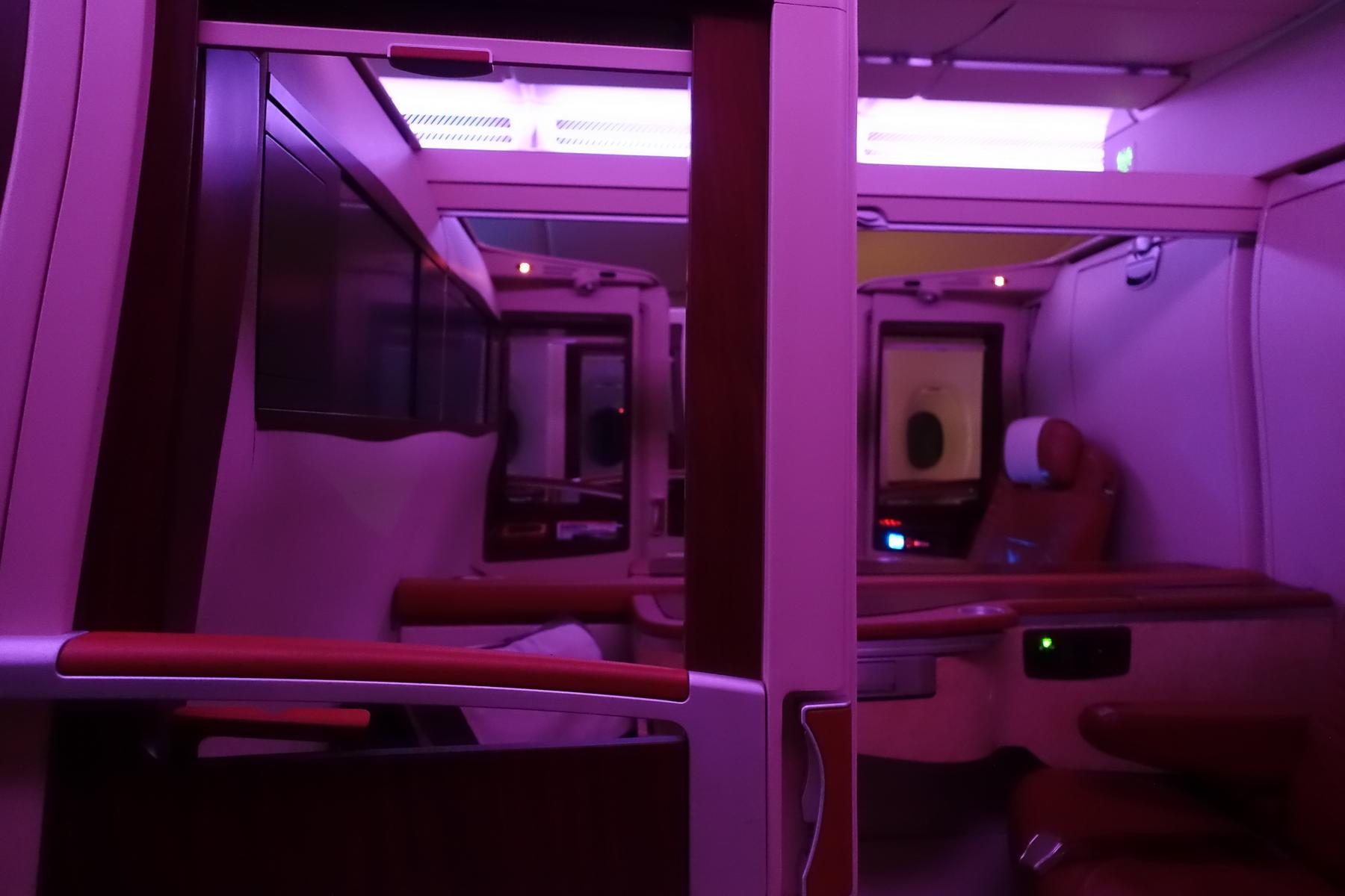 Singapore Airlines Suites Class cabin with two individual suites illuminated by purple light.