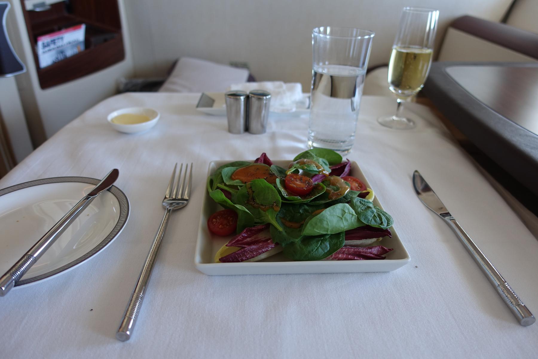 A neatly presented salad, water, and champagne on a white tablecloth in a Singapore Airlines First Class suite.